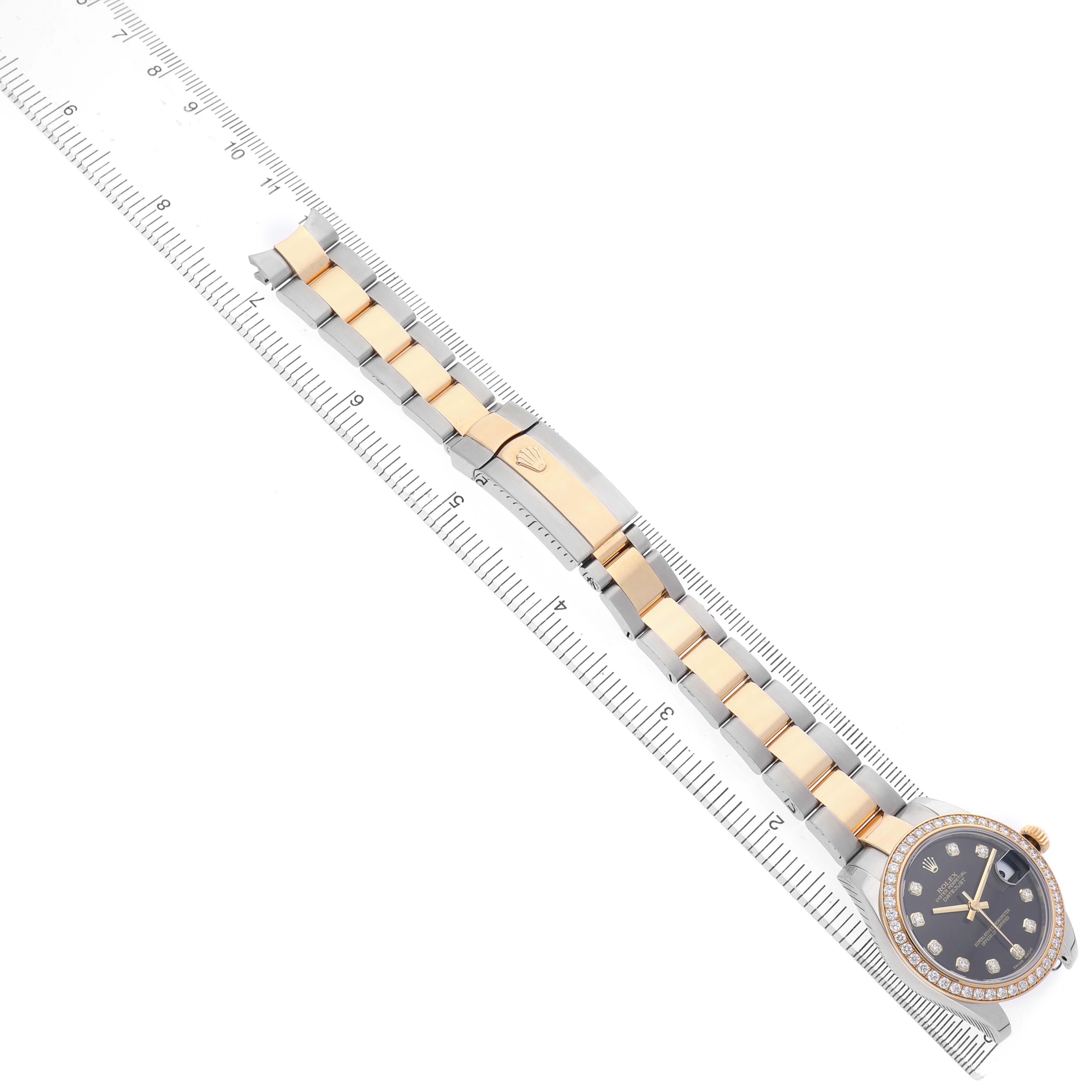 The image shows a Rolex Datejust 178383 Women's Steel and Gold (two tone) Black Dial watch from an angled top view, highlighting the bracelet and the clasp on a ruler for scale.