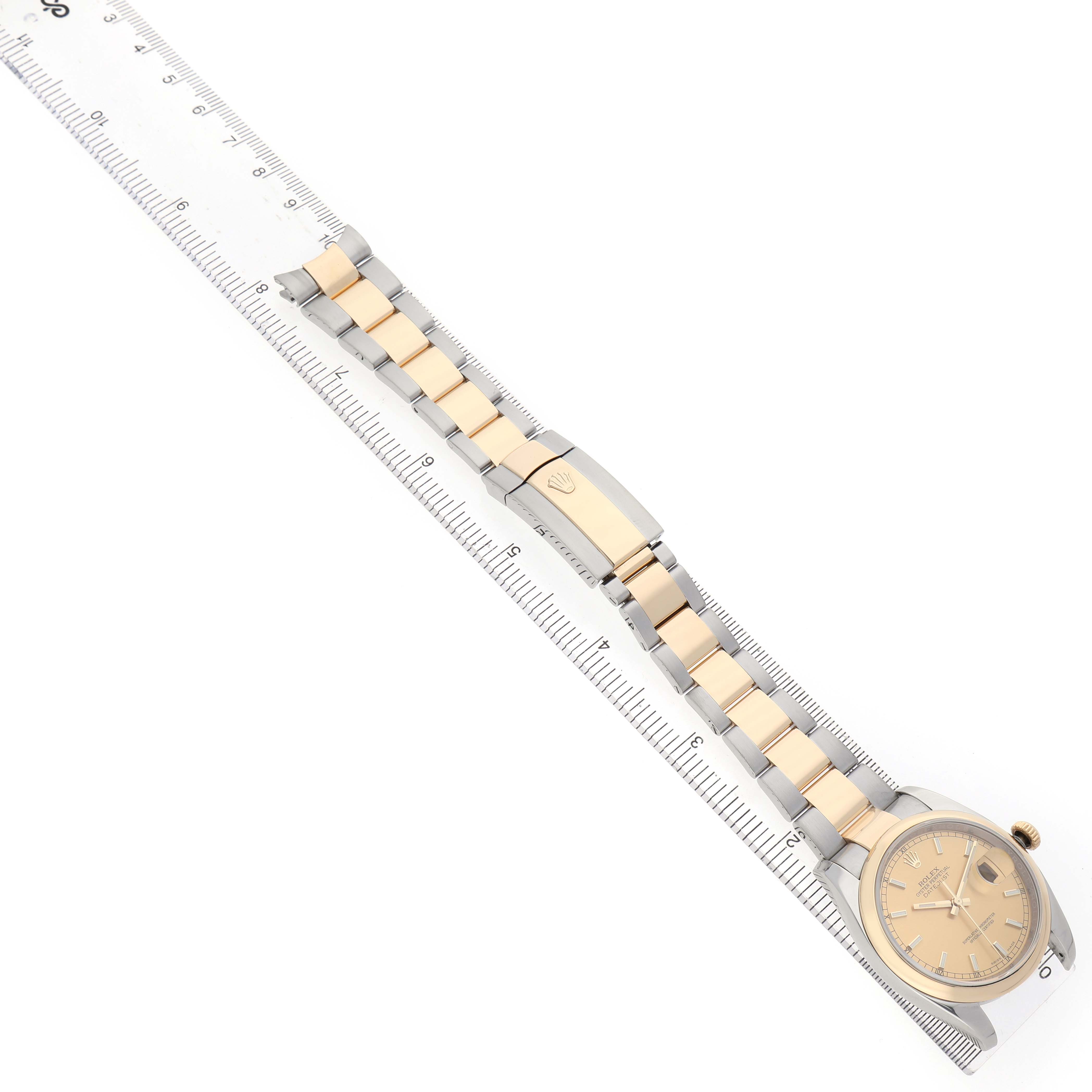 The Rolex Datejust 116203 Men's Stainless Steel Champagne Dial watch is shown from a top-down angle, displaying the face, bracelet, and clasp alongside a ruler.