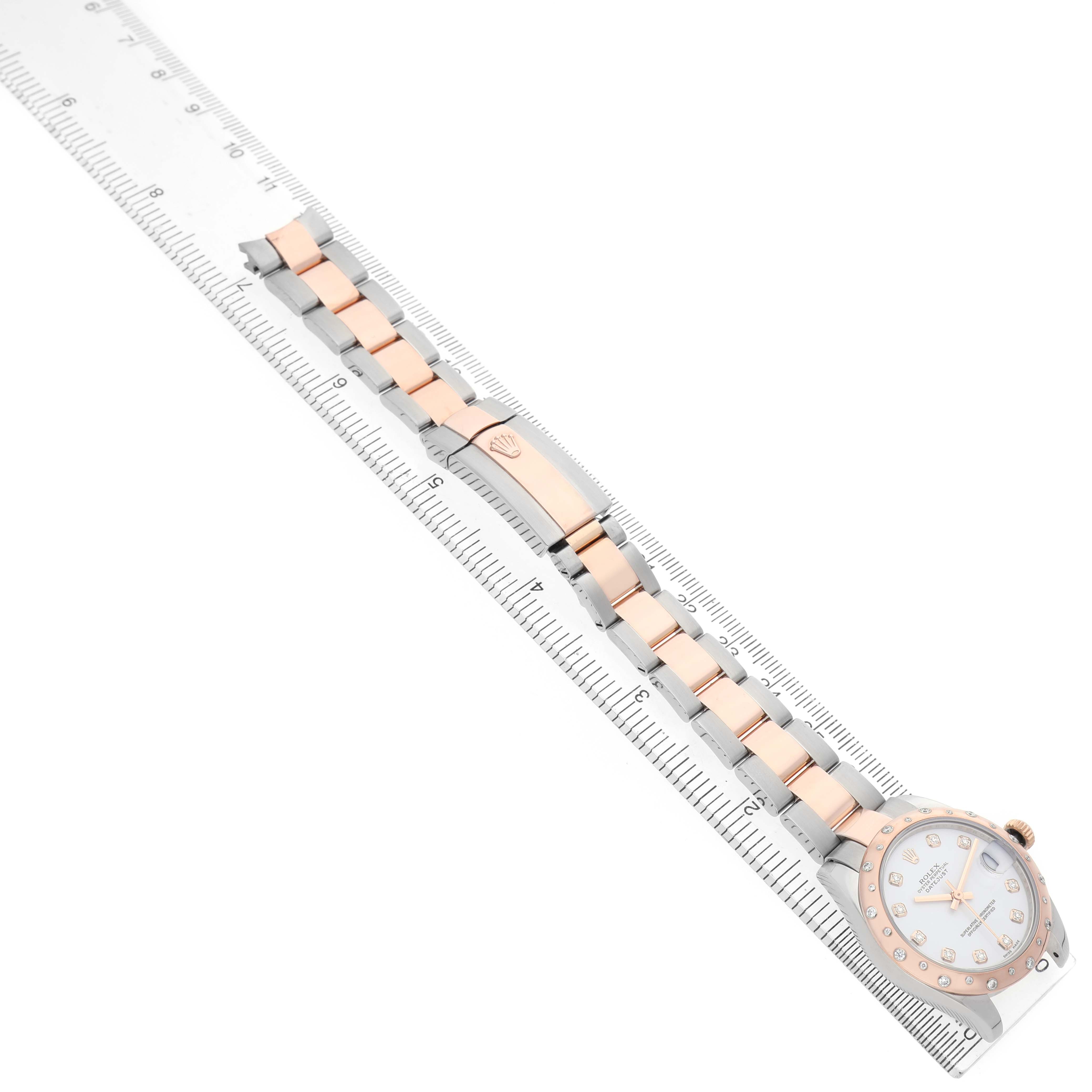The Rolex Datejust 178341 Women's Steel and Gold (two tone) White Dial watch is shown from an overhead angle, highlighting the bracelet and clasp placed alongside a ruler for scale.