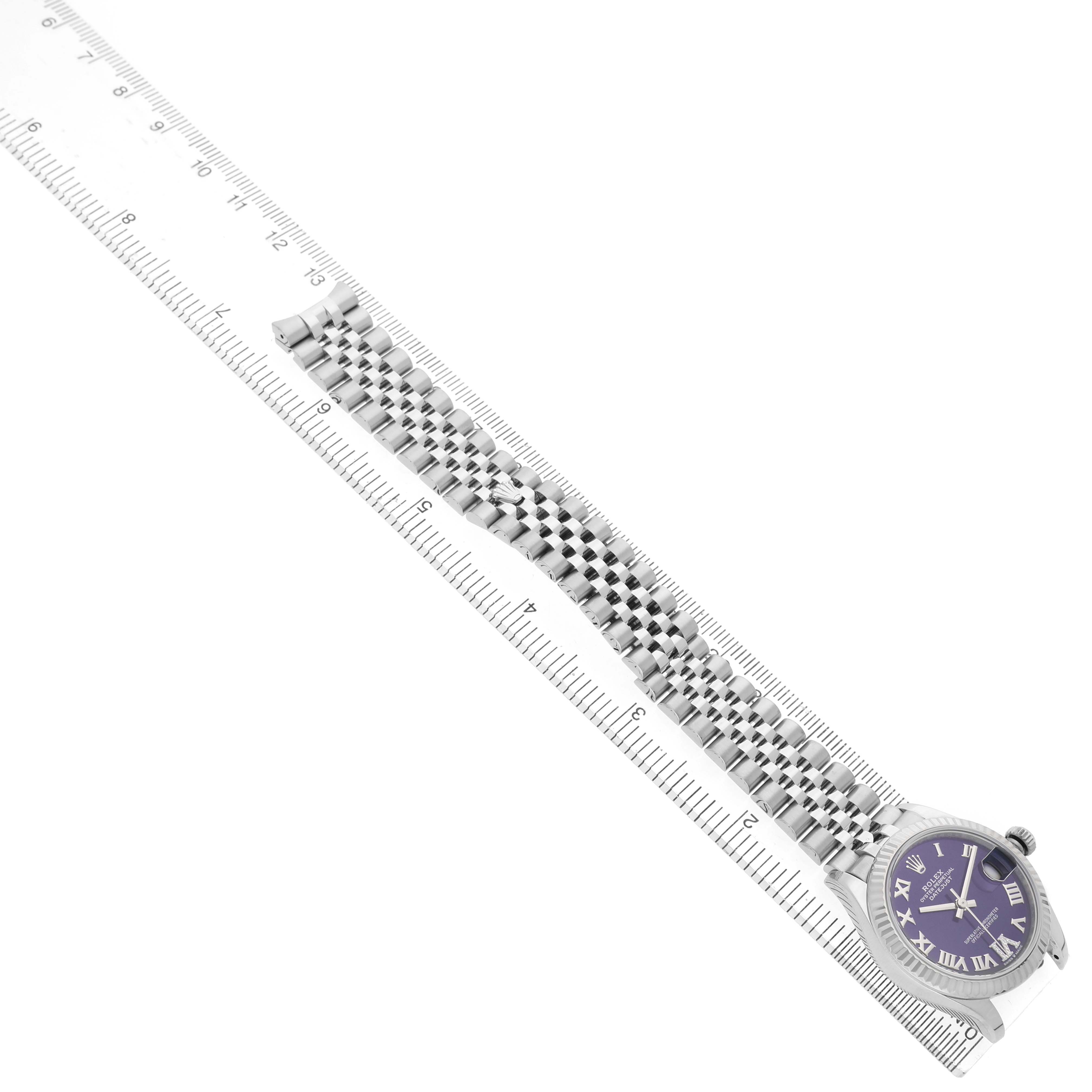 The Rolex Datejust 278274 Women's Stainless Steel Purple Dial watch is shown from an elevated side angle, displaying the face, bezel, and metal bracelet alongside a ruler.