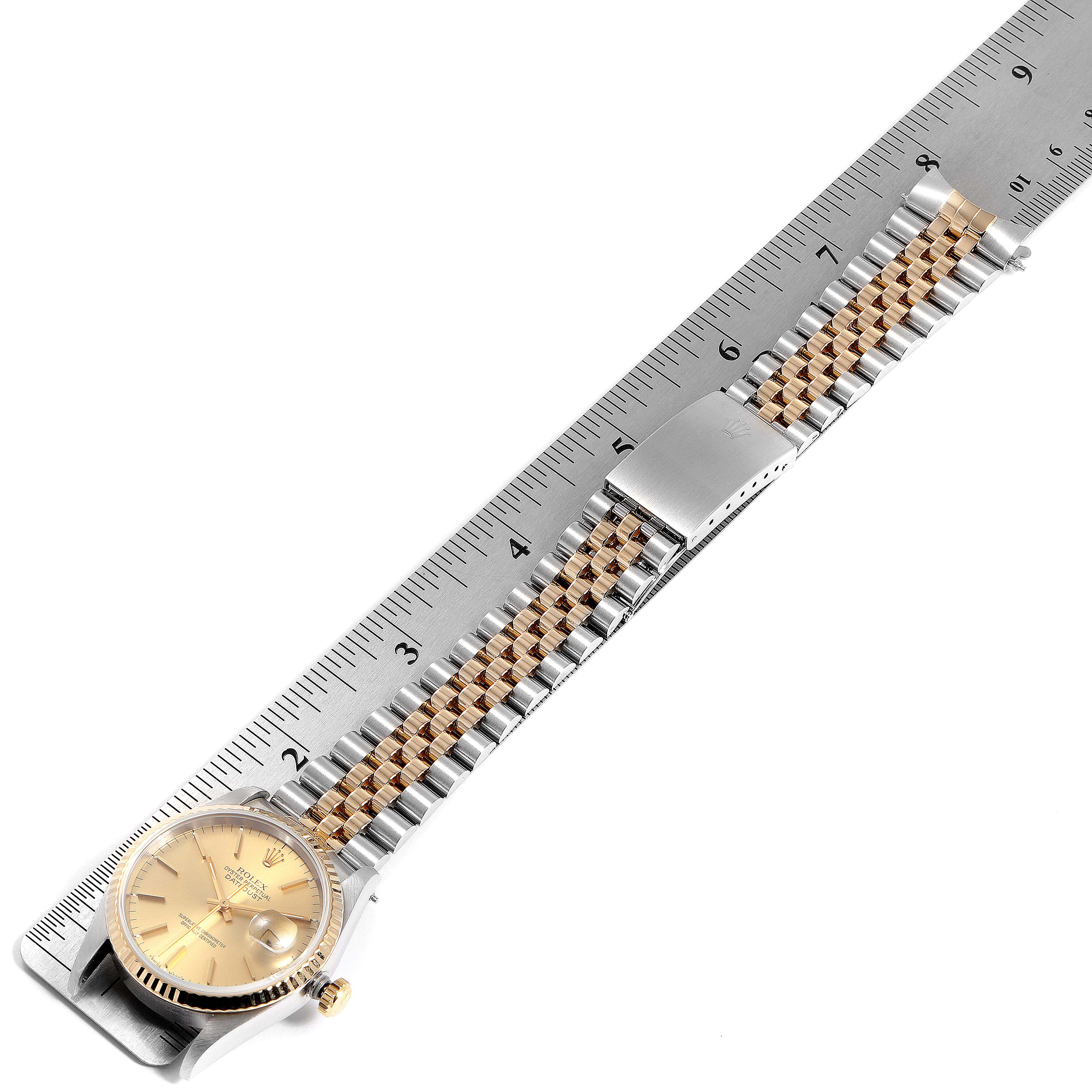 The Rolex Datejust 16233 Men
s Steel and Gold (two tone) Champagne Dial 16233 Men
s Steel and Gold (two tone) Champagne Dial watch is shown from a top-down angle, highlighting its face, bracelet, and clasp, alongside a ruler for scale.