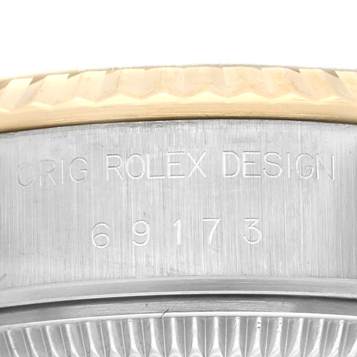 This close-up image shows the side of a Rolex Datejust 69173 Women's Steel and Gold (two tone) Champagne Dial 69173 Women's Steel and Gold (two tone) Champagne Dial watch case with the model number 69173 and "ORIG ROLEX DESIGN" engraved.