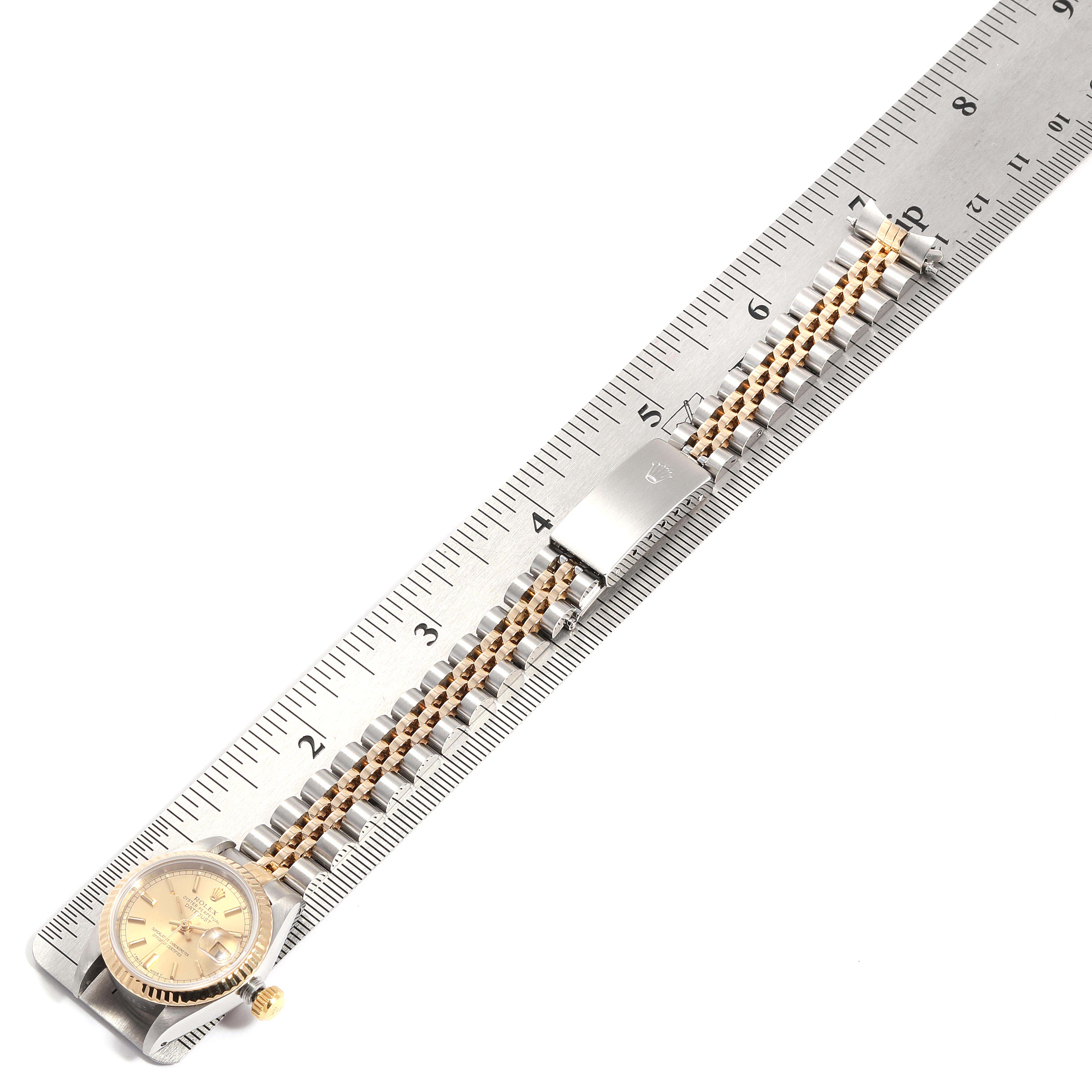The image shows the Rolex Datejust 69173 Women
s Steel and Gold (two tone) Champagne Dial 69173 Women
s Steel and Gold (two tone) Champagne Dial watch and its band along a ruler, positioned at an angle highlighting the face and Jubilee bracelet.