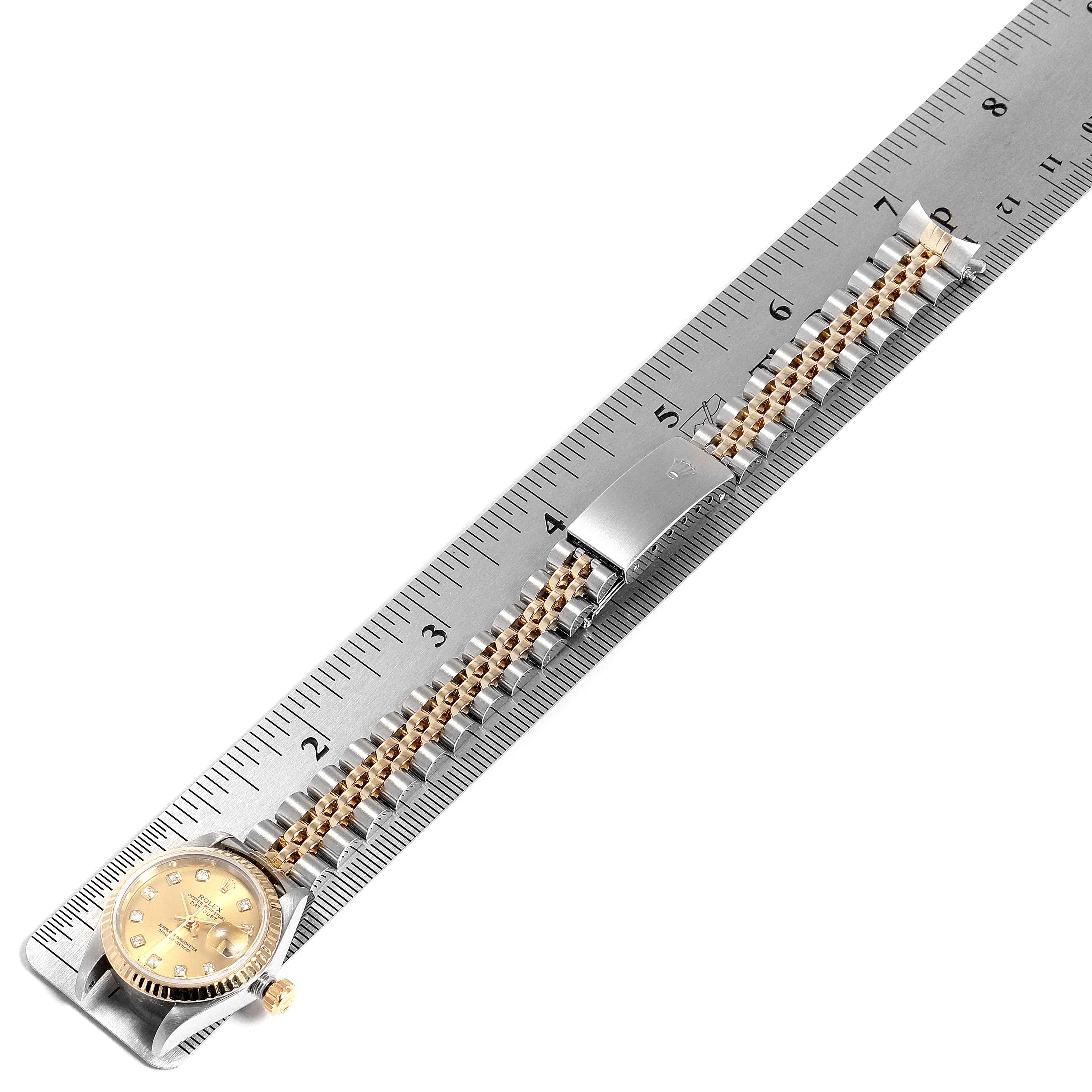The image shows a Rolex Datejust 79173 Women's Steel and Gold (two tone) Champagne Dial 79173 Women's Steel and Gold (two tone) Champagne Dial watch laid flat on a ruler, displaying the face, crown, and bracelet.