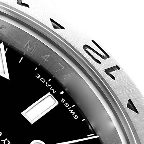 The image shows a close-up of the Rolex Explorer 216570 Men
s Stainless Steel Black Dial watch, focusing on the bezel with its engraved numbers and part of the black dial.