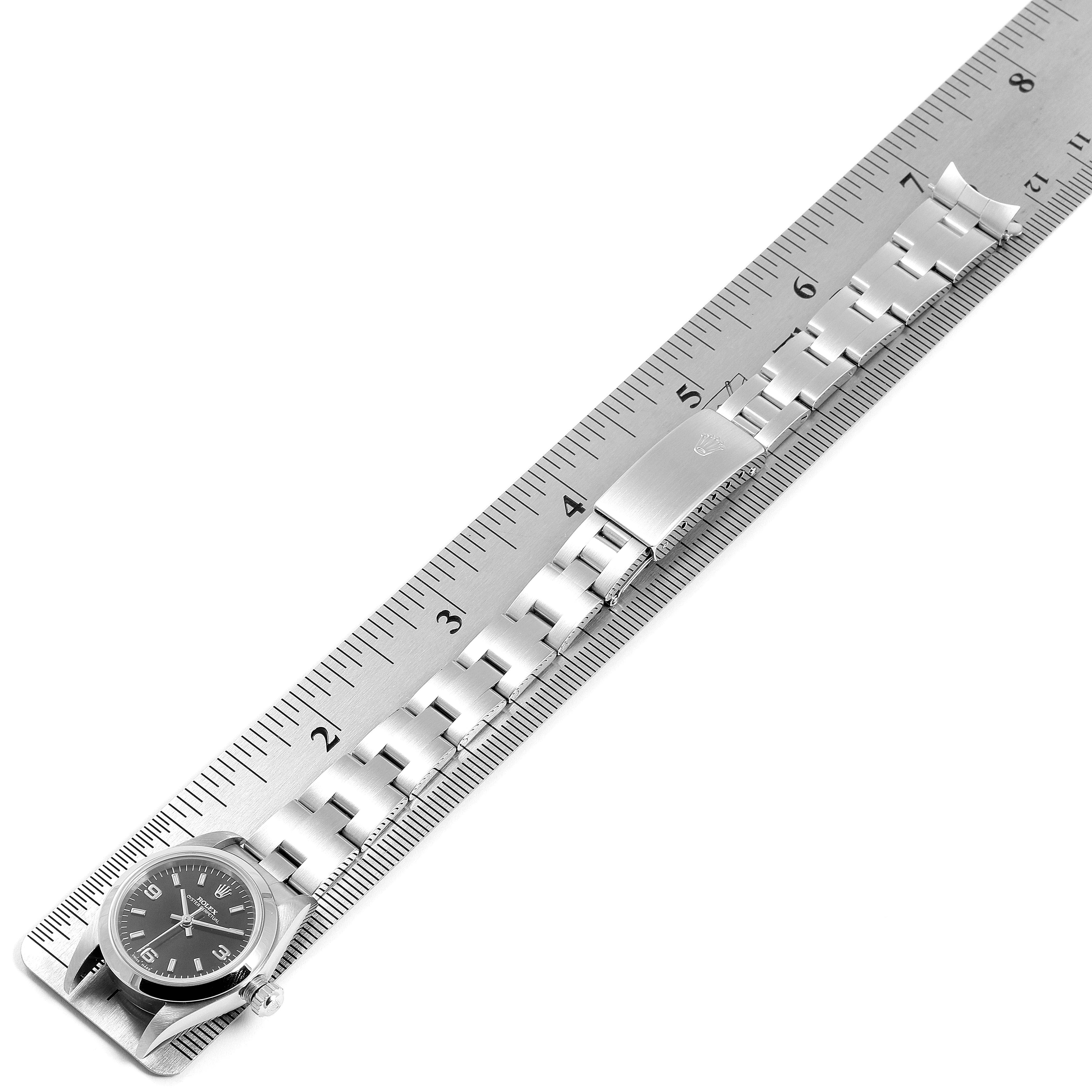 The image shows a top-down view of a Rolex Oyster Perpetual 76080 Women
s Stainless Steel Black Dial 76080 Women
s Stainless Steel Black Dial watch with its stainless steel bracelet next to a ruler.