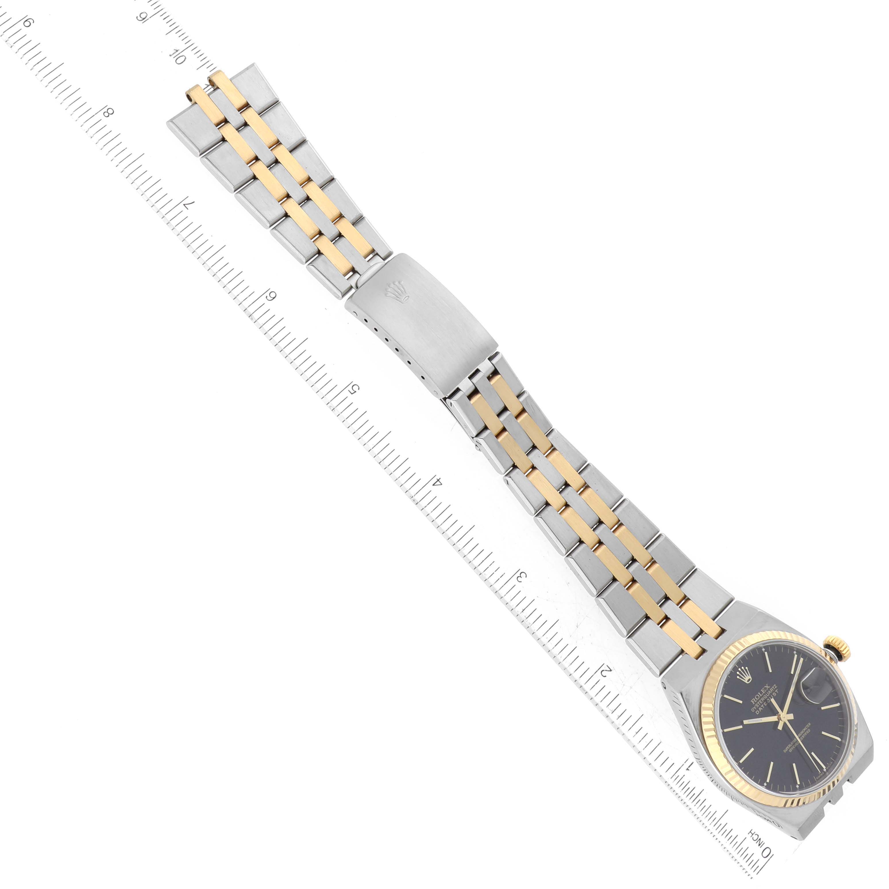 The Rolex Oysterquartz 17013 Men
s Steel and Gold (two tone) Black Dial 17013 Men
s Steel and Gold (two tone) Black Dial watch is shown laid flat, featuring the full bracelet, clasp, and dial, with a ruler for scale.