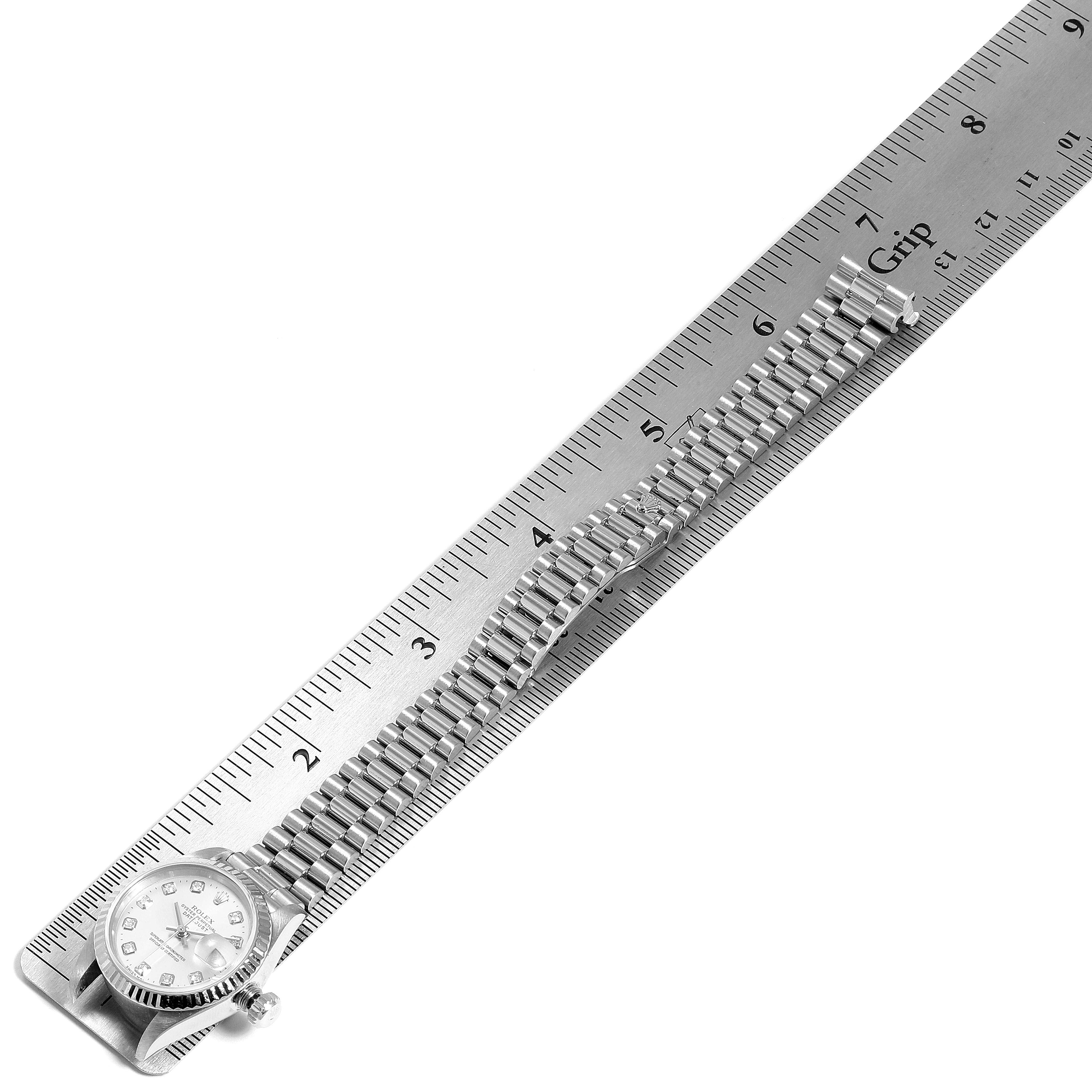 The image shows a Rolex President 69179 Women
s White Gold Silver Dial 69179 Women
s White Gold Silver Dial model watch viewed from above, with the bracelet fully extended alongside a ruler.