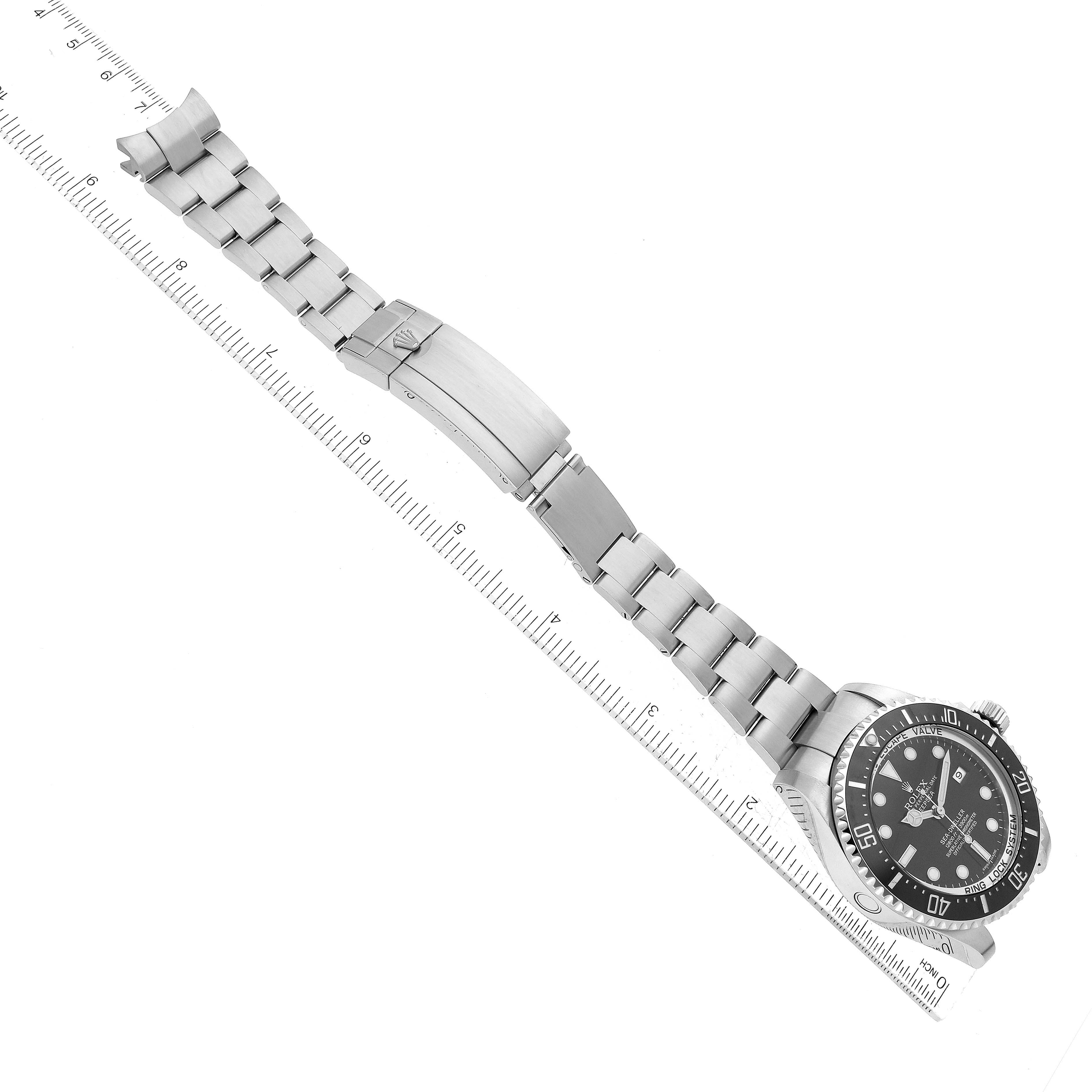 This Rolex Sea-Dweller 116660 Men
s Stainless Steel Black Dial 116660 Men
s Stainless Steel Black Dial watch is shown from an overhead angle, highlighting its face, bezel, bracelet, and clasp, with a ruler for scale.