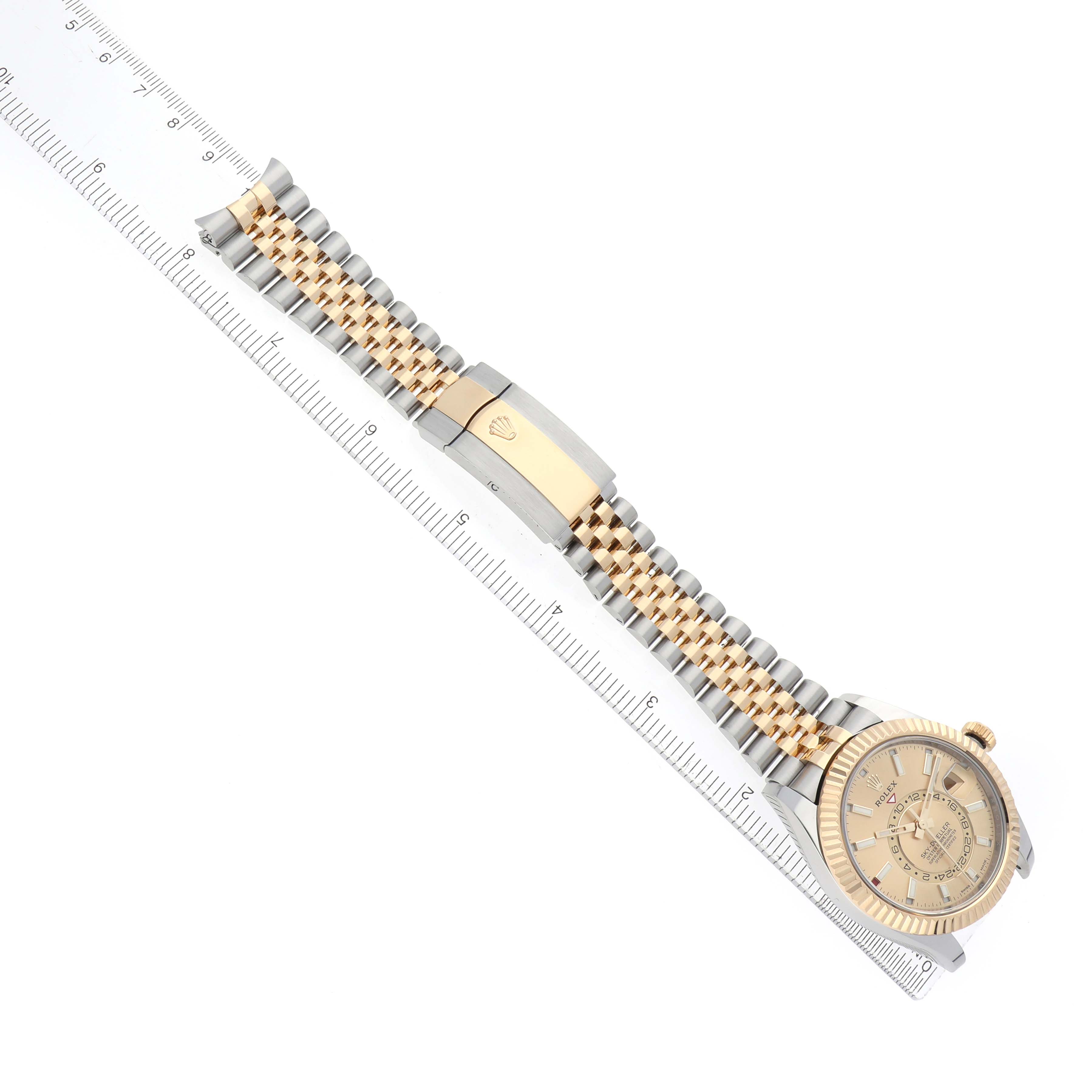The Rolex Sky-Dweller 3269333 Men
s Steel and Gold (two tone) Champagne Dial watch is shown from an angled top view, featuring its face, bracelet, and clasp beside a ruler for scale.