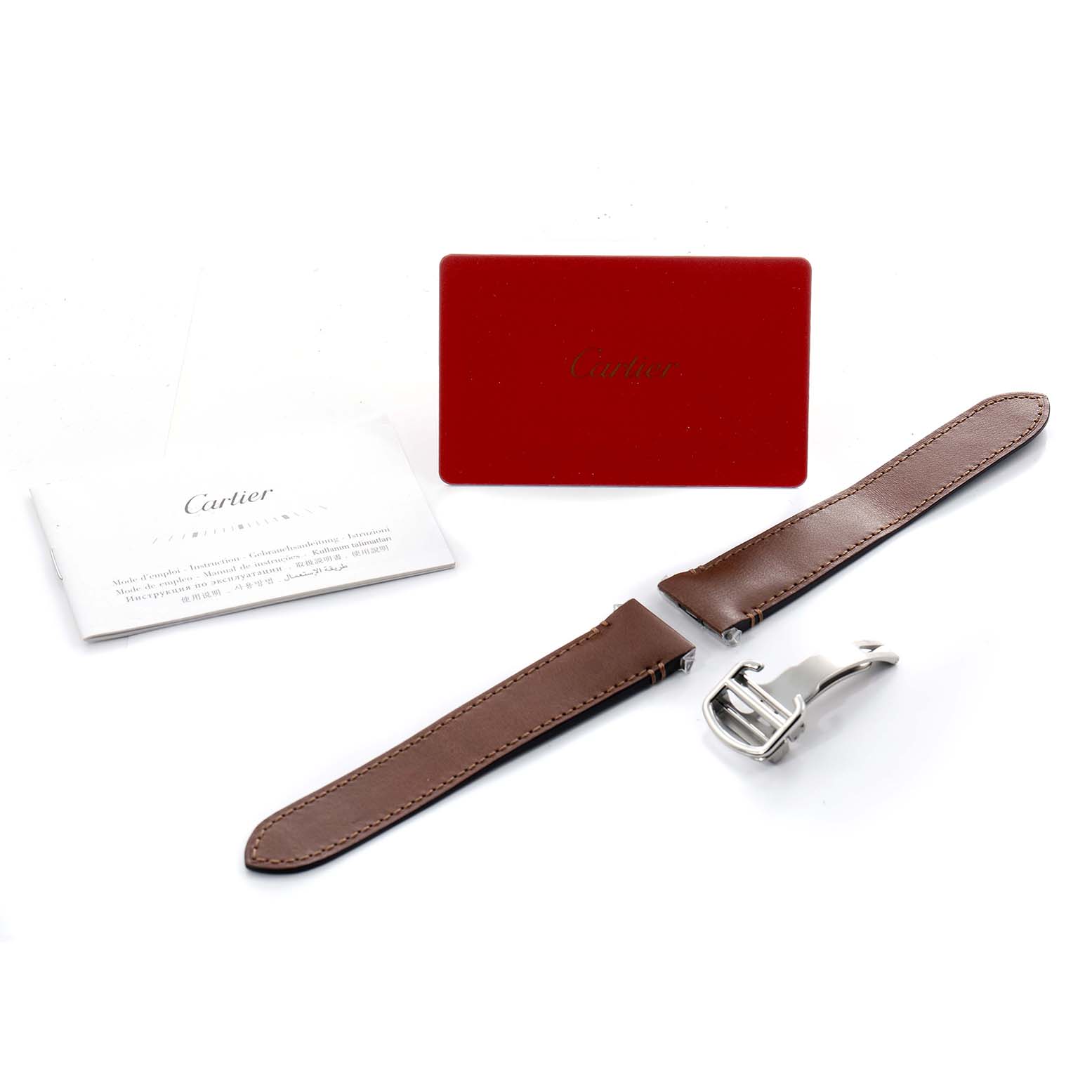 The image shows a brown leather strap and a clasp for the Cartier Santos W2SA0009 Men
s Stainless Steel Silver Dial model, alongside a red card and a manual.