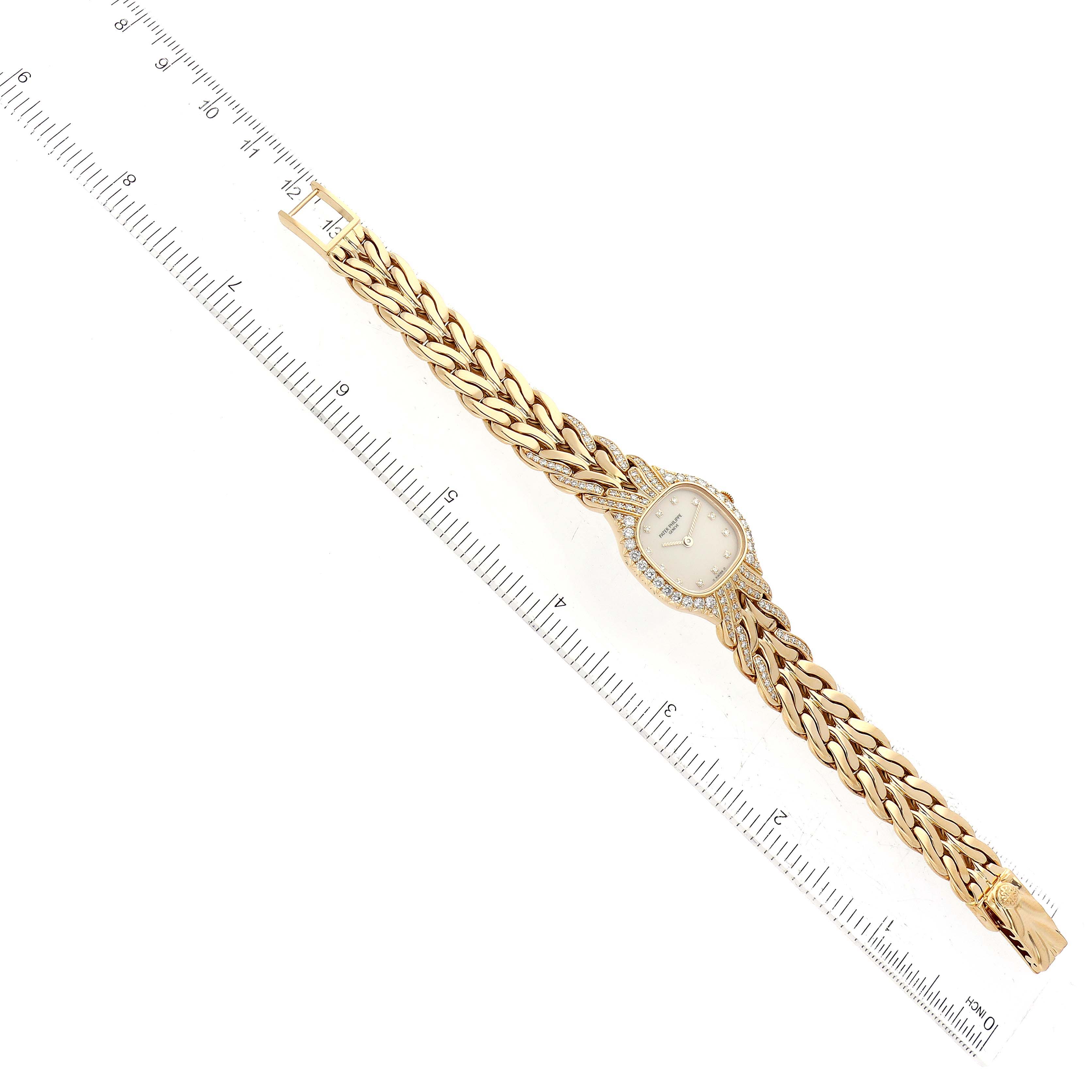 The La Flamme model by Patek Philippe is shown from a top-down angle, displaying the dial, bezel, and full bracelet with a measuring ruler.