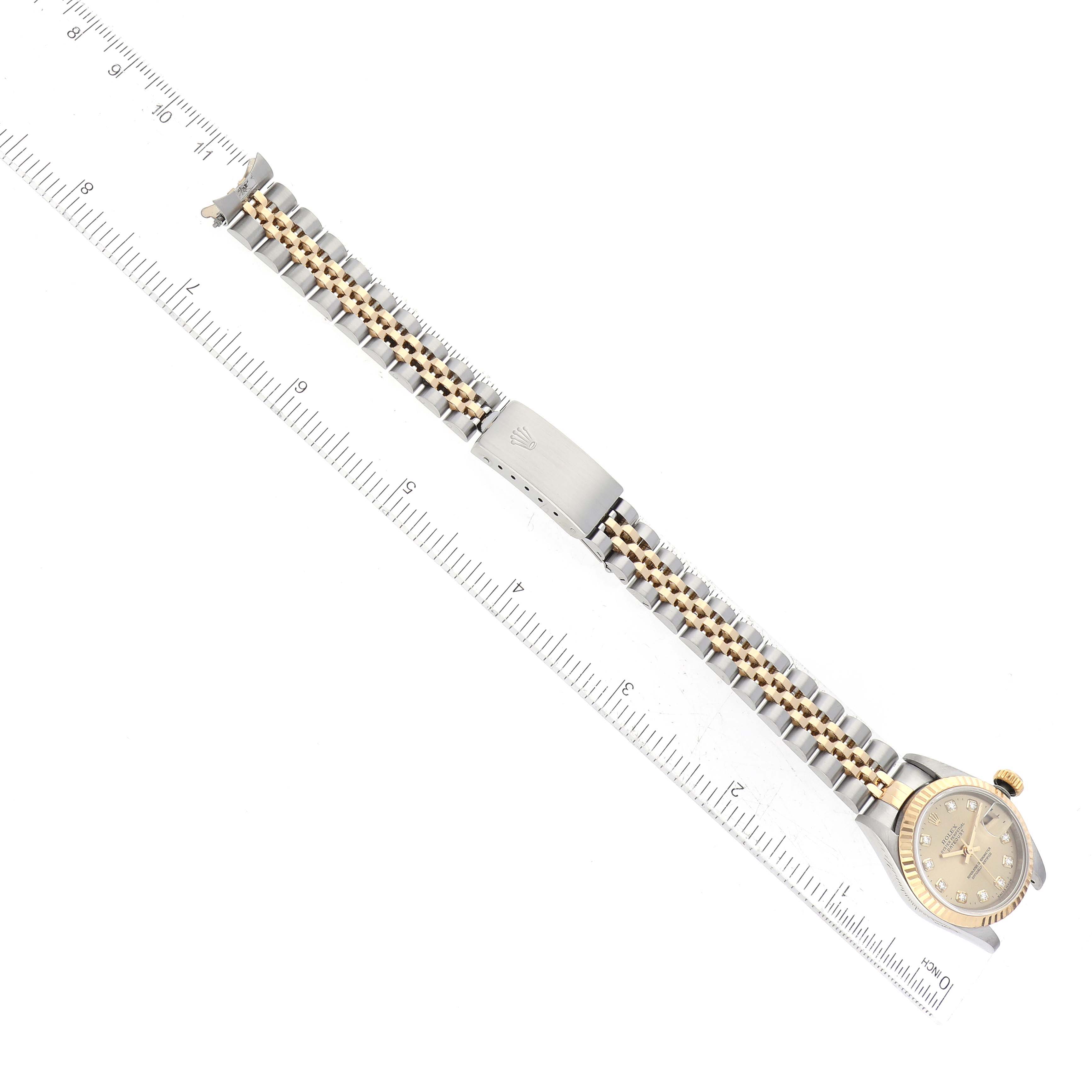 This image shows the Rolex Datejust 69173 Women's Steel and Gold (two tone) Champagne Dial 69173 Women's Steel and Gold (two tone) Champagne Dial watch laid flat alongside a ruler, displaying the entire bracelet, clasp, and face.