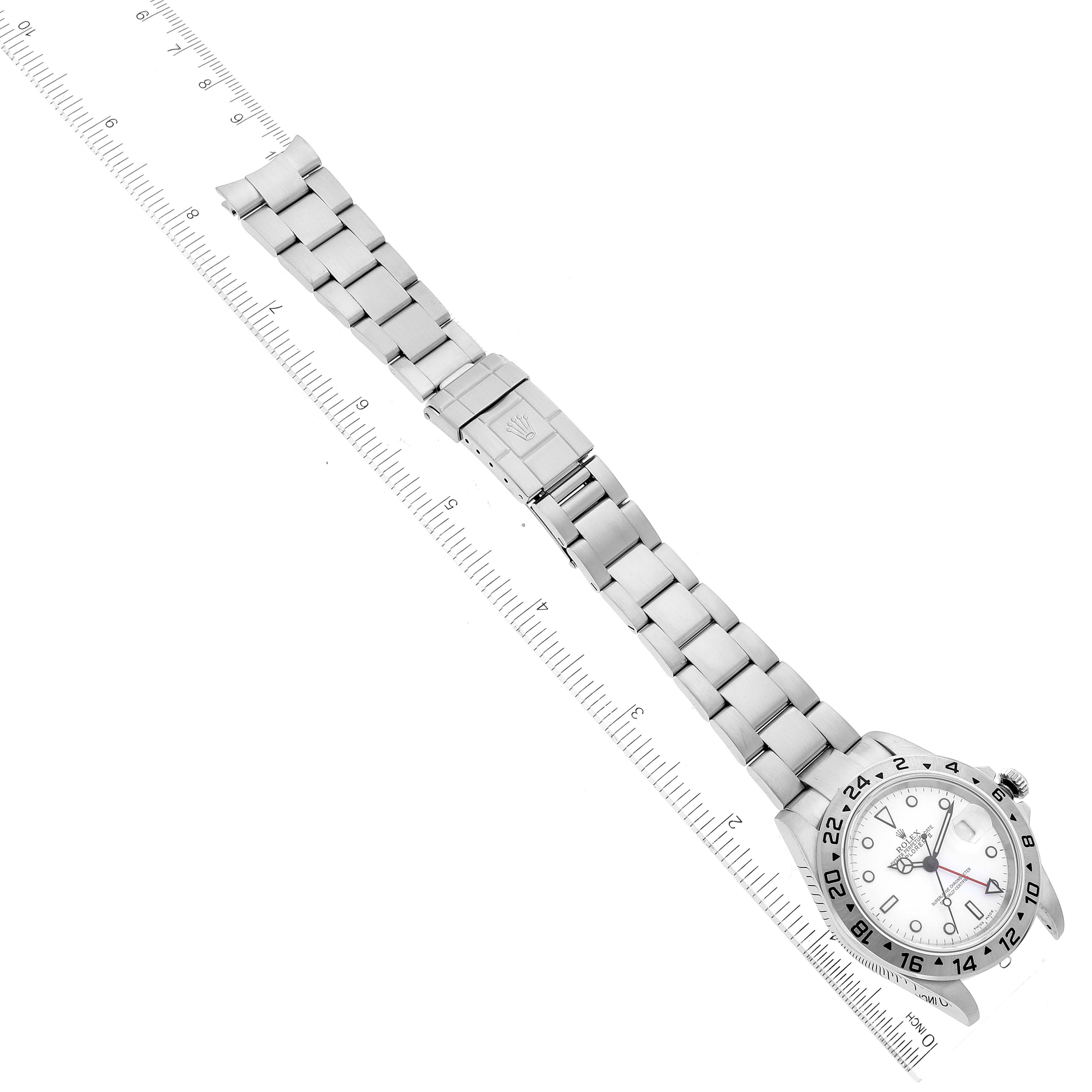 The Rolex Explorer 16570 Men's Stainless Steel White Dial 16570 Men's Stainless Steel White Dial watch is shown flat, from an overhead view, with its metal band extended alongside a ruler.