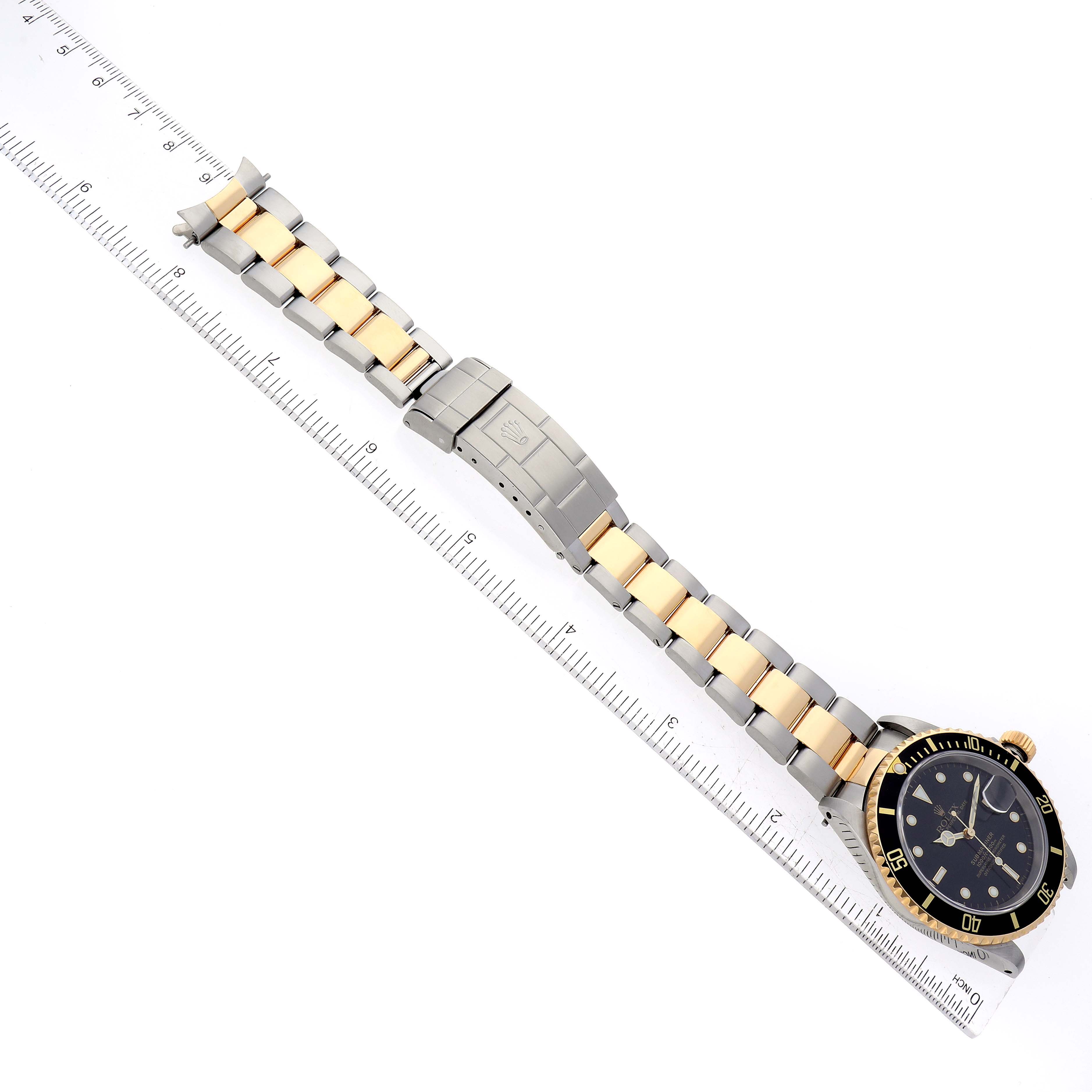 This image shows a Rolex Submariner 16613 Men's Steel and Gold (two tone) Black Dial 16613 Men's Steel and Gold (two tone) Black Dial watch laid flat on a ruler, displaying its full bracelet, clasp, and face from a top-down perspective.