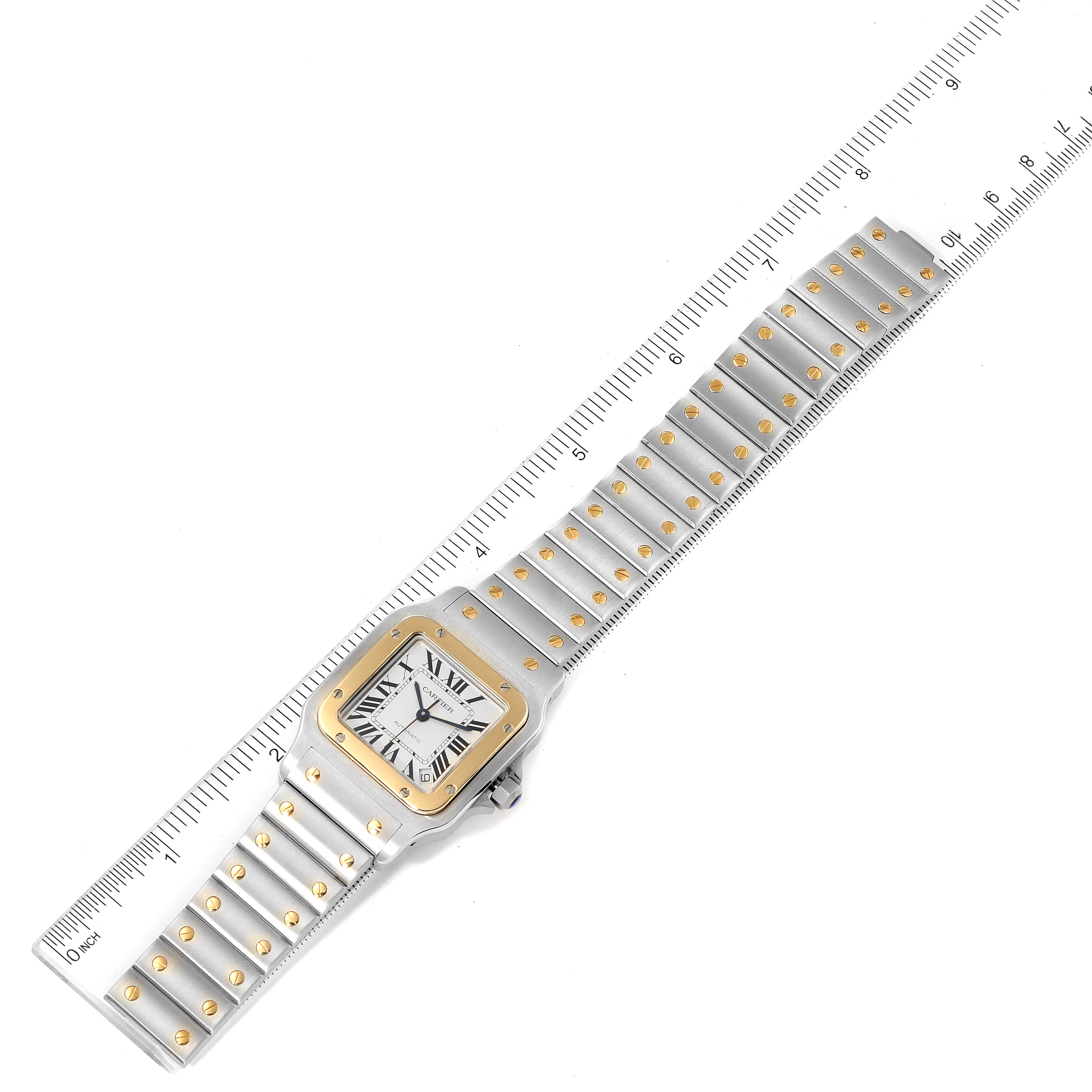 The Cartier Santos W20099C4 Men
s Steel and Gold (two tone) Silver Dial W20099C4 Men
s Steel and Gold (two tone) Silver Dial watch is shown from a top-down angle, highlighting its bracelet and square face with a ruler for scale.