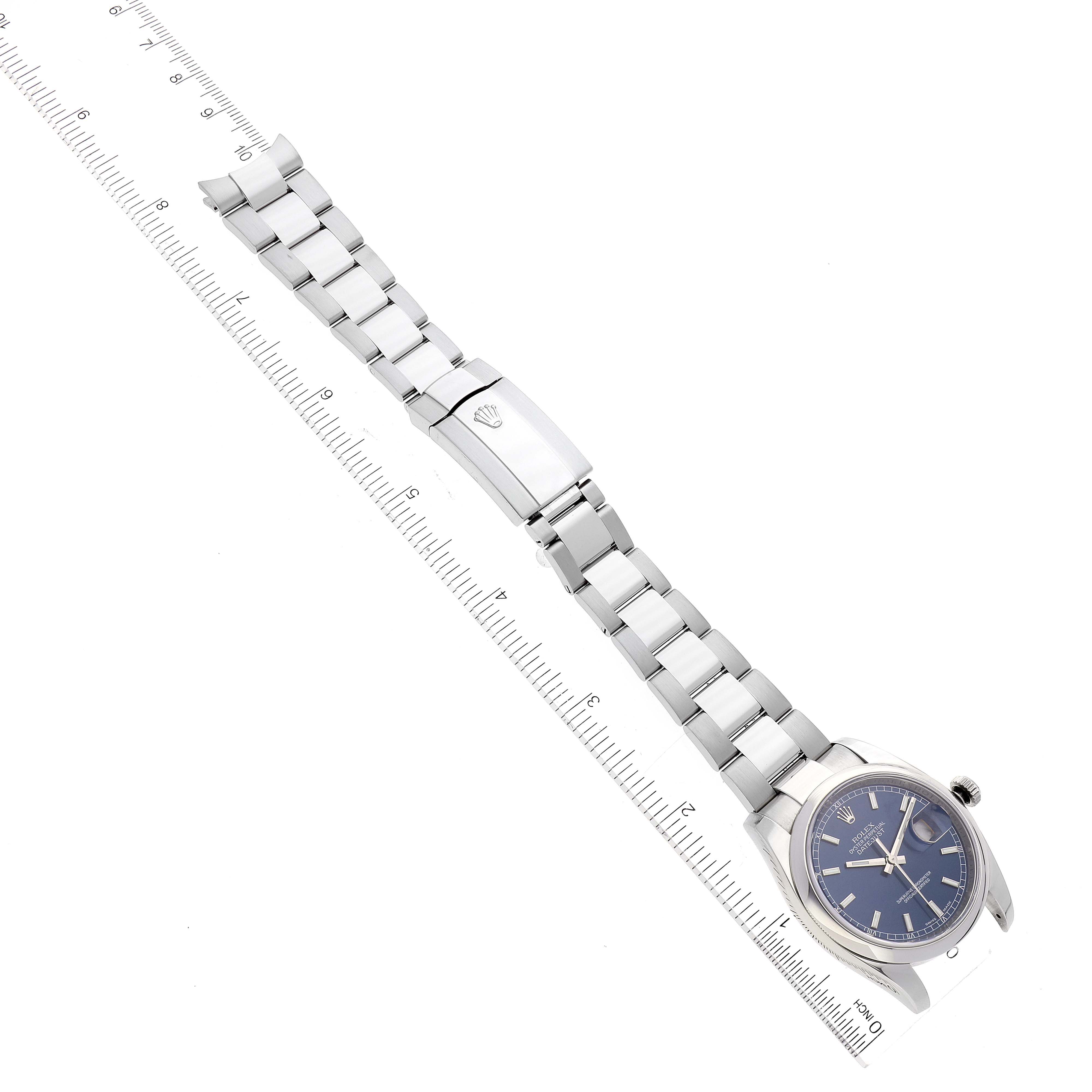 The image shows a Rolex Datejust 116200 Men's Stainless Steel Blue Dial 116200 Men's Stainless Steel Blue Dial watch laid flat on a ruler, displaying the face, bracelet, clasp, and part of the crown.