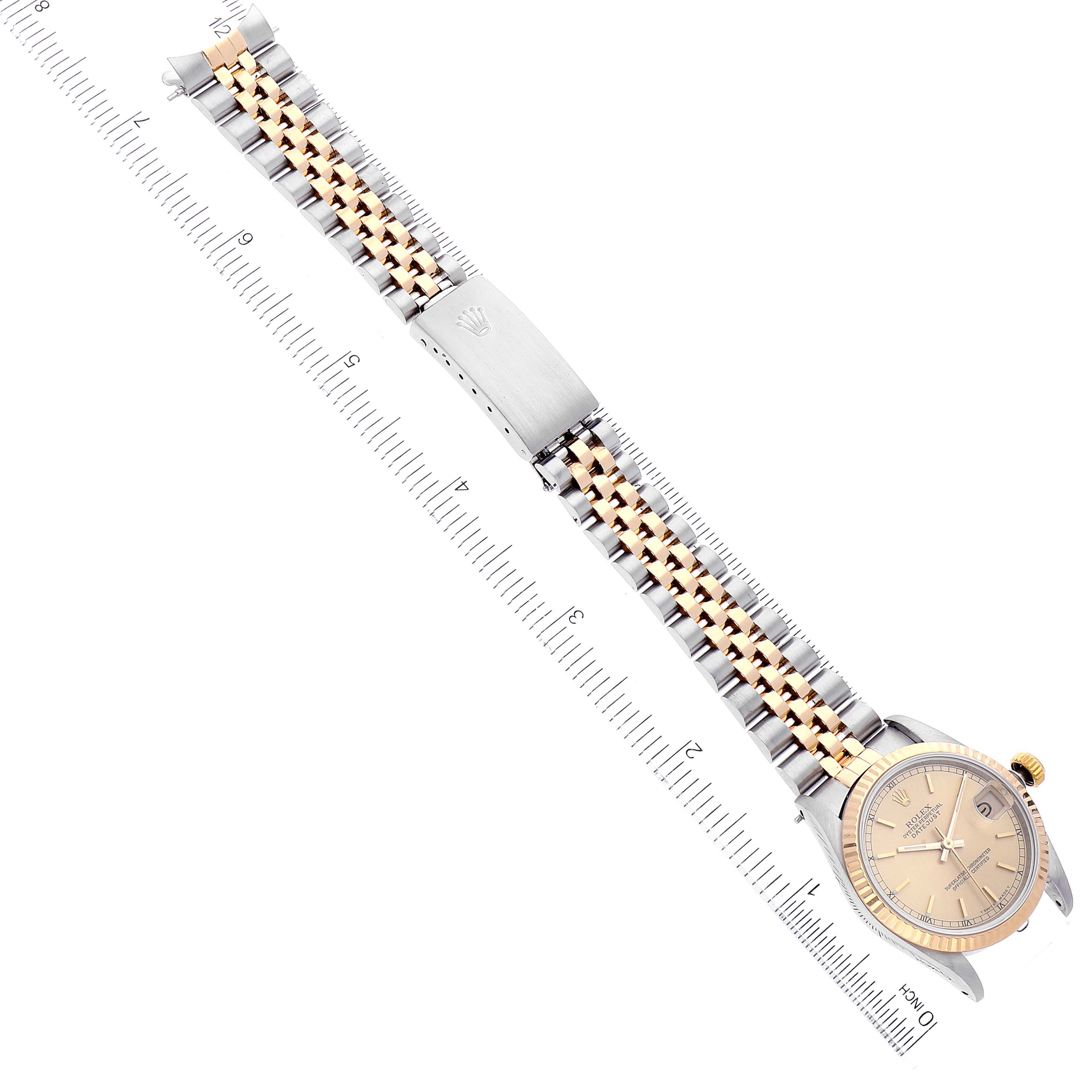 The image shows an overhead view of a Rolex Mid-Size 68273 Women
s Steel and Gold (two tone) Champagne Dial 68273 Women
s Steel and Gold (two tone) Champagne Dial watch, displaying the dial, bezel, bracelet, and clasp next to a ruler.