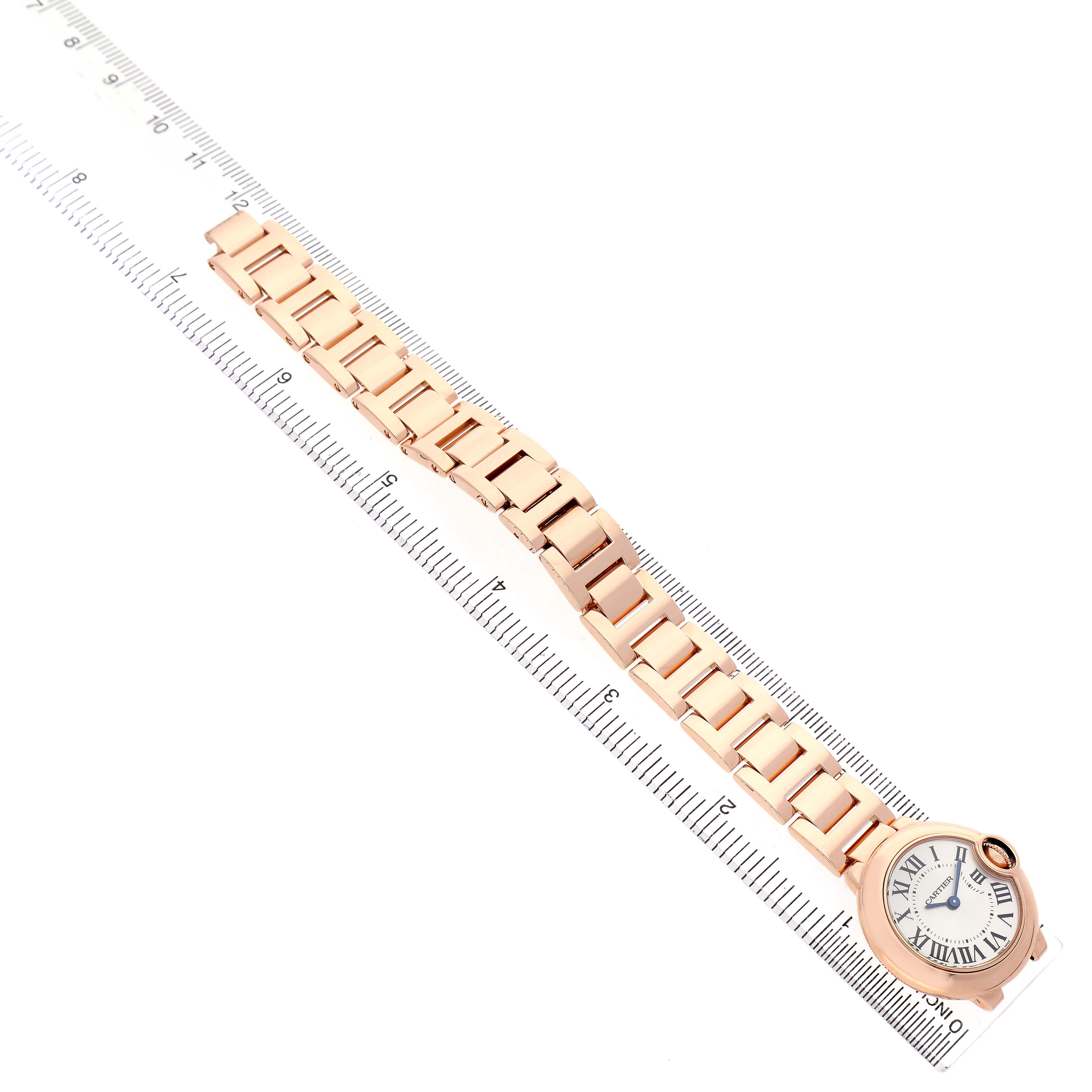 The image shows a Ballon Bleu de Cartier watch horizontally laid on a ruler, highlighting its bracelet and face.