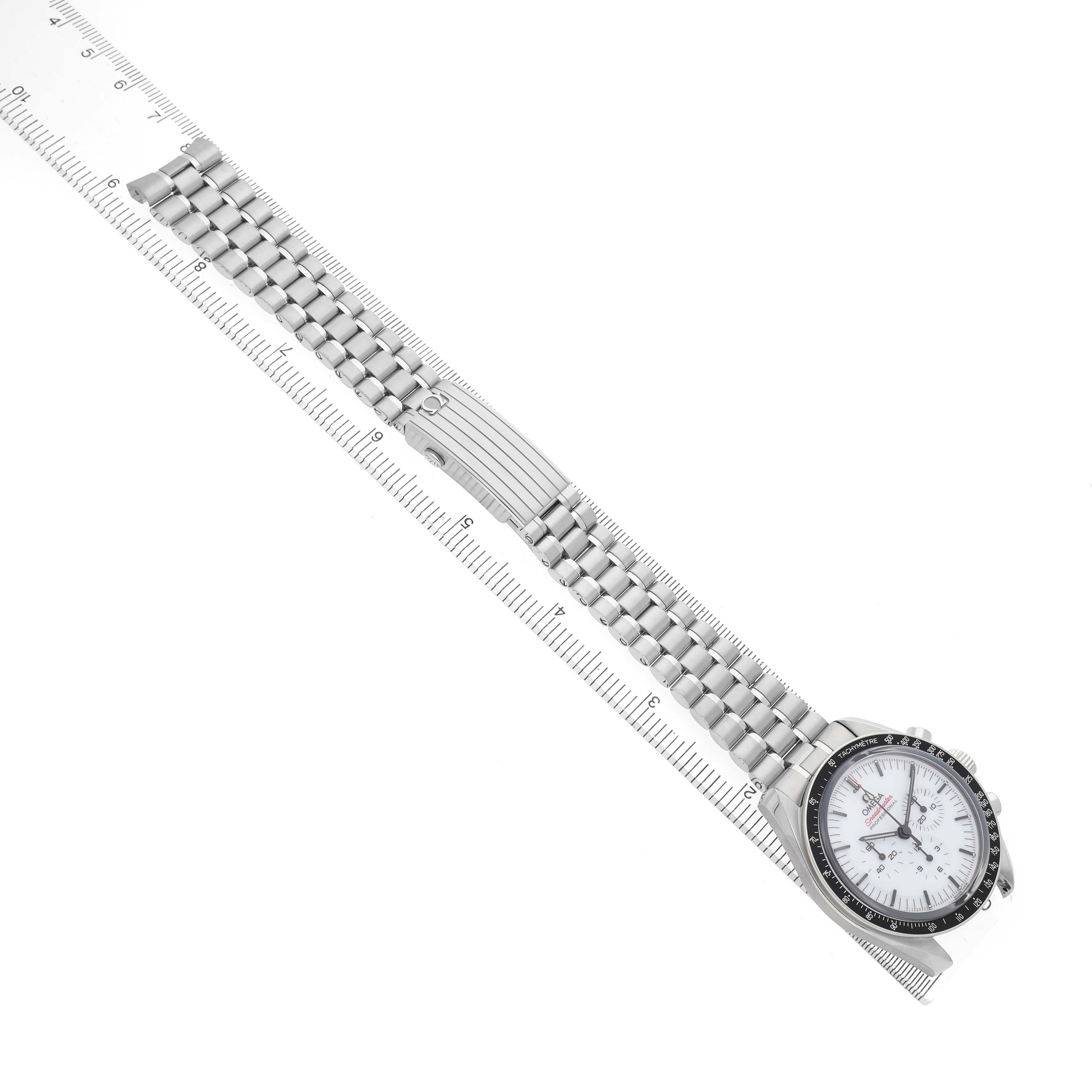 The Omega Speedmaster 310.30.42.50.04.001 Men's Stainless Steel White Dial watch is shown from an overhead angle, displaying the full bracelet and face alongside a ruler.