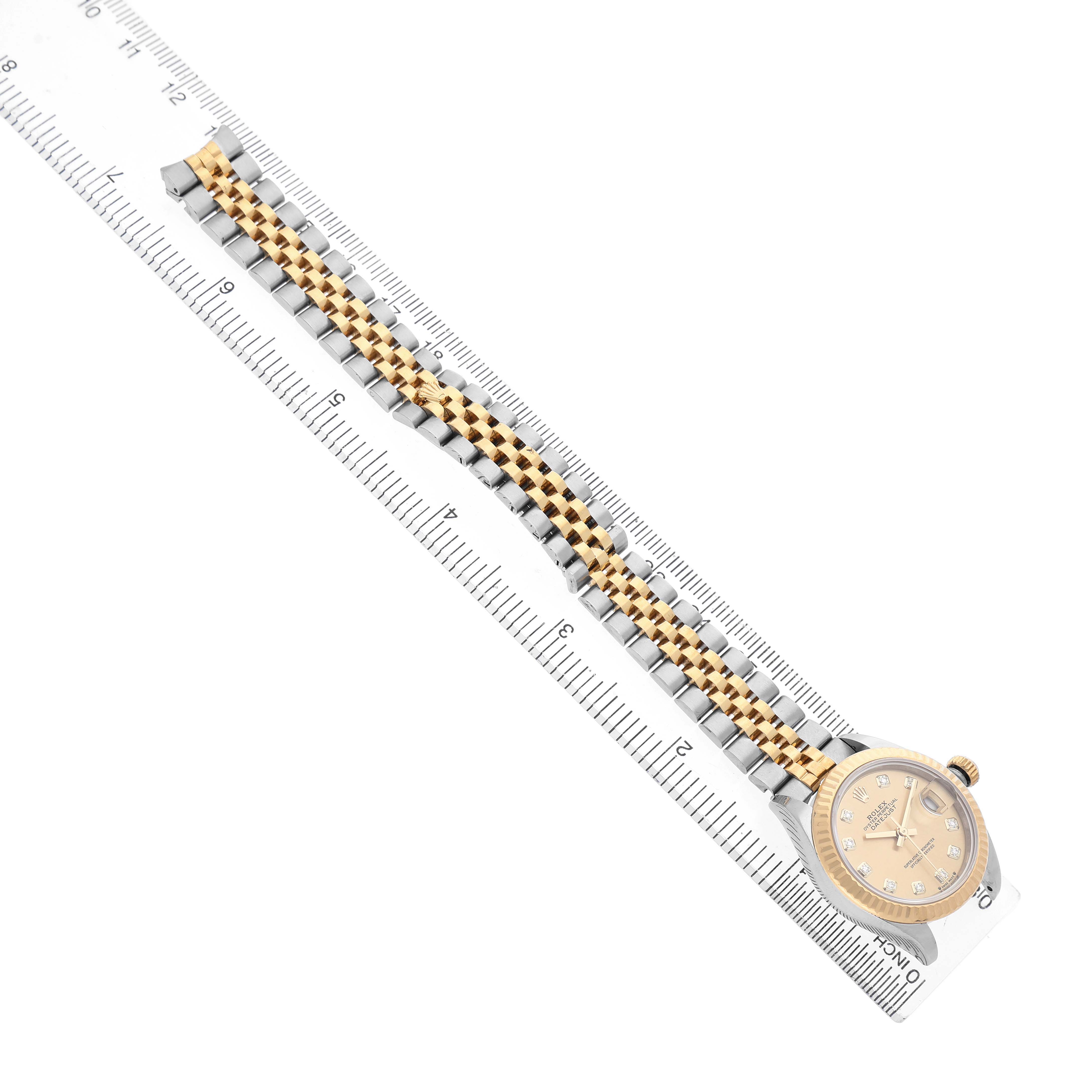 The Rolex Datejust 279173 Women's Steel and Gold (two tone) Champagne Dial watch is shown from an overhead angle, displaying the full bracelet against a ruler.