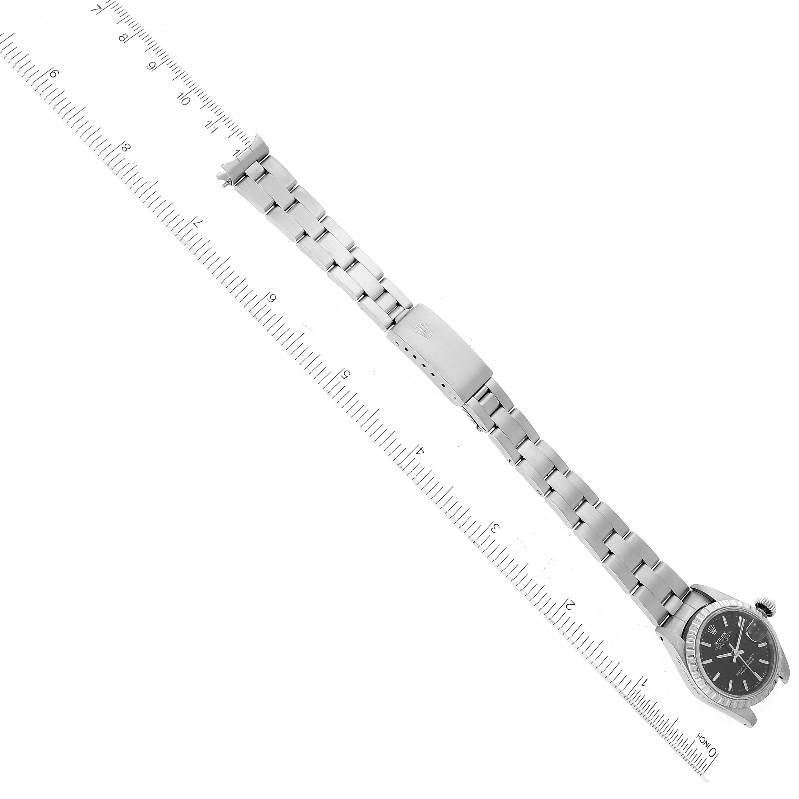 The Rolex Datejust 69240 Women's Stainless Steel Black Dial 69240 Women's Stainless Steel Black Dial watch is shown from a top-down angle, displaying the face, bracelet, and clasp beside a ruler.