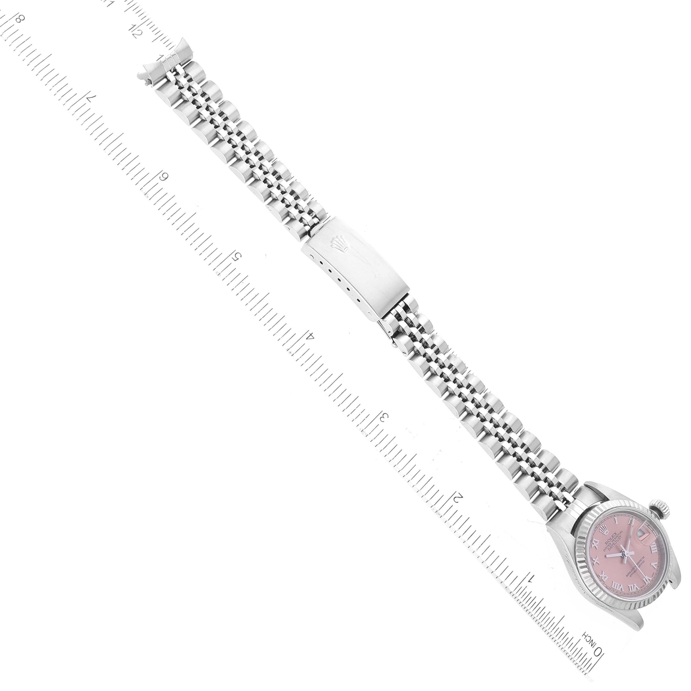This image shows a Rolex Datejust 79174 Women's Stainless Steel Pink Dial 79174 Women's Stainless Steel Pink Dial watch laid flat, featuring its oystersteel case, pink dial, jubilee bracelet, and a ruler for scale.