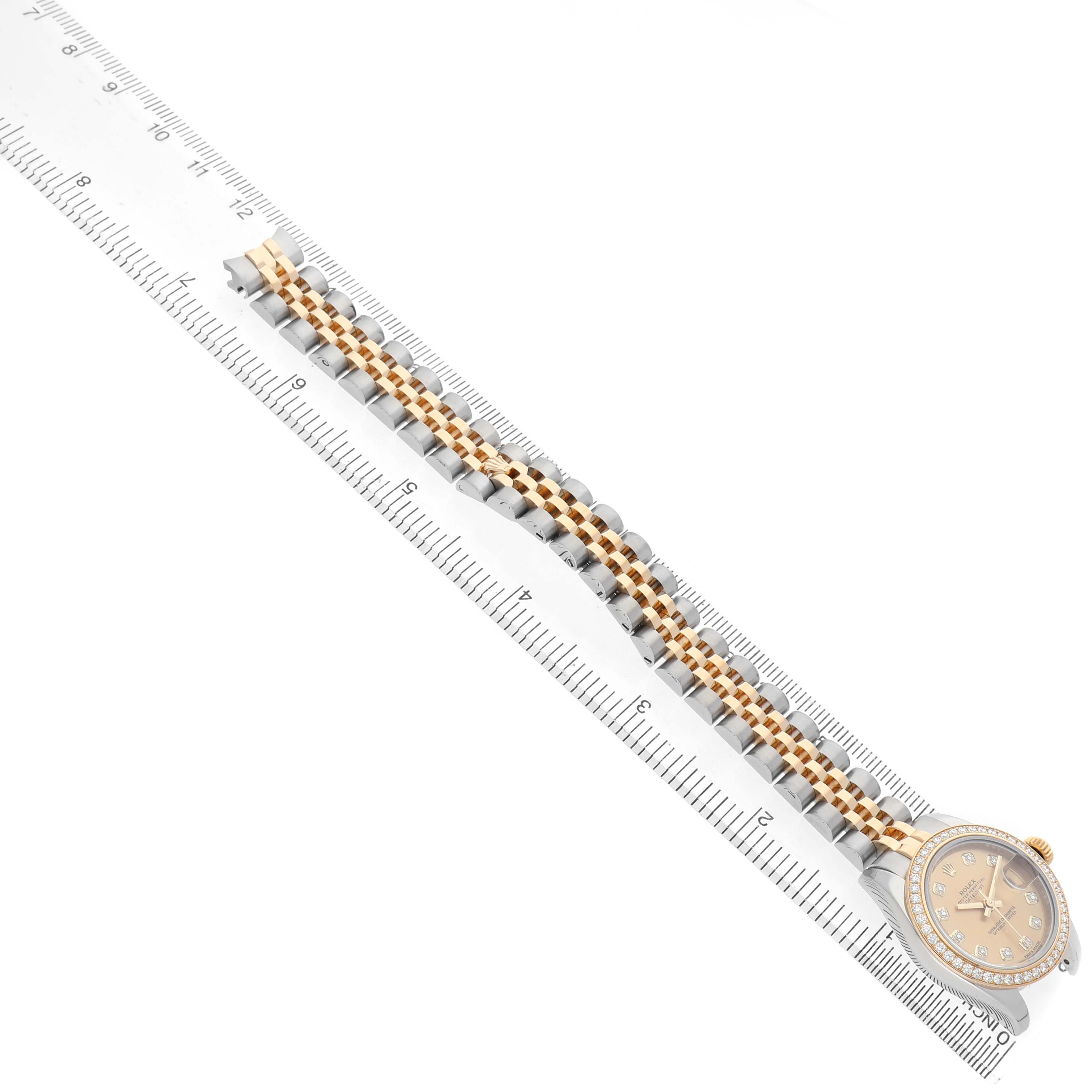 The Rolex Datejust 179383 Women's Steel and Gold (two tone) Champagne Dial watch is shown from a top-down angle, highlighting its face and two-tone bracelet alongside a ruler.