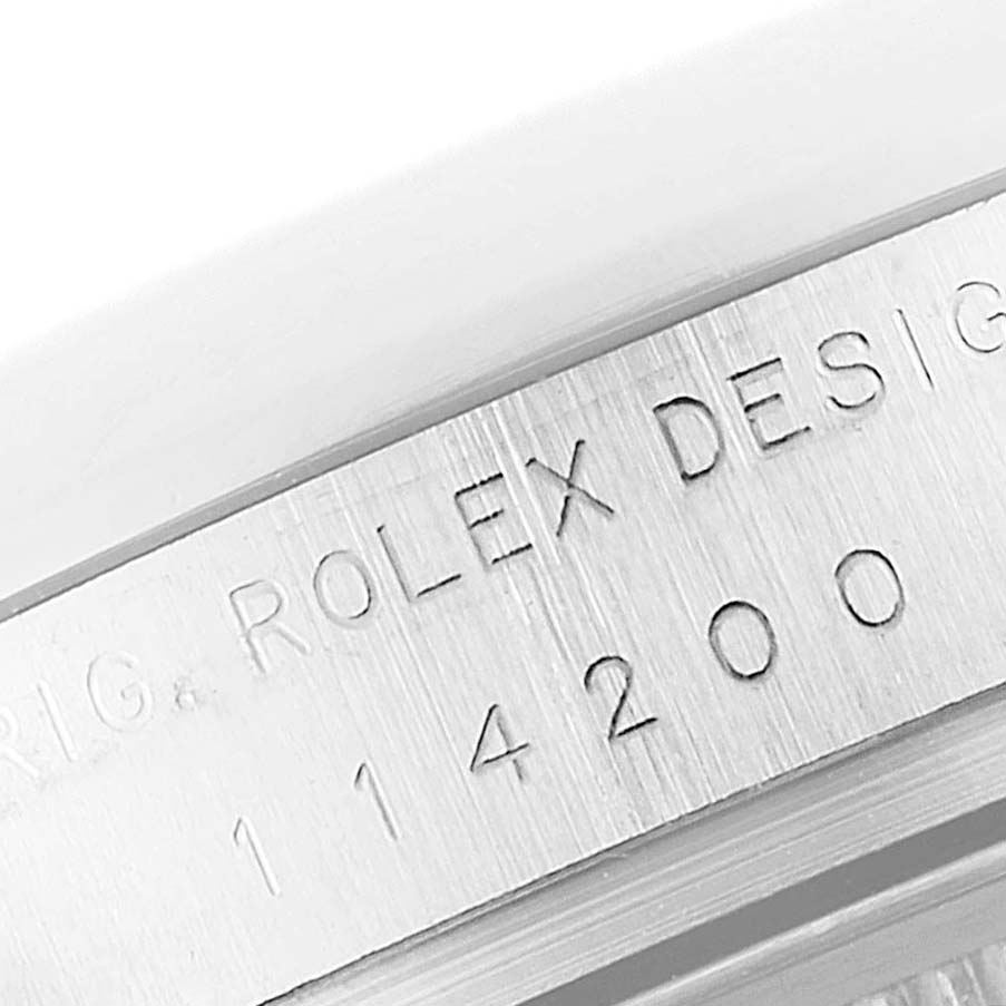 This image shows a close-up of the engraved serial number and brand markings on the side of the Rolex Oyster Perpetual 114200 Men's Stainless Steel Champagne Dial 114200 Men's Stainless Steel Champagne Dial watch case.