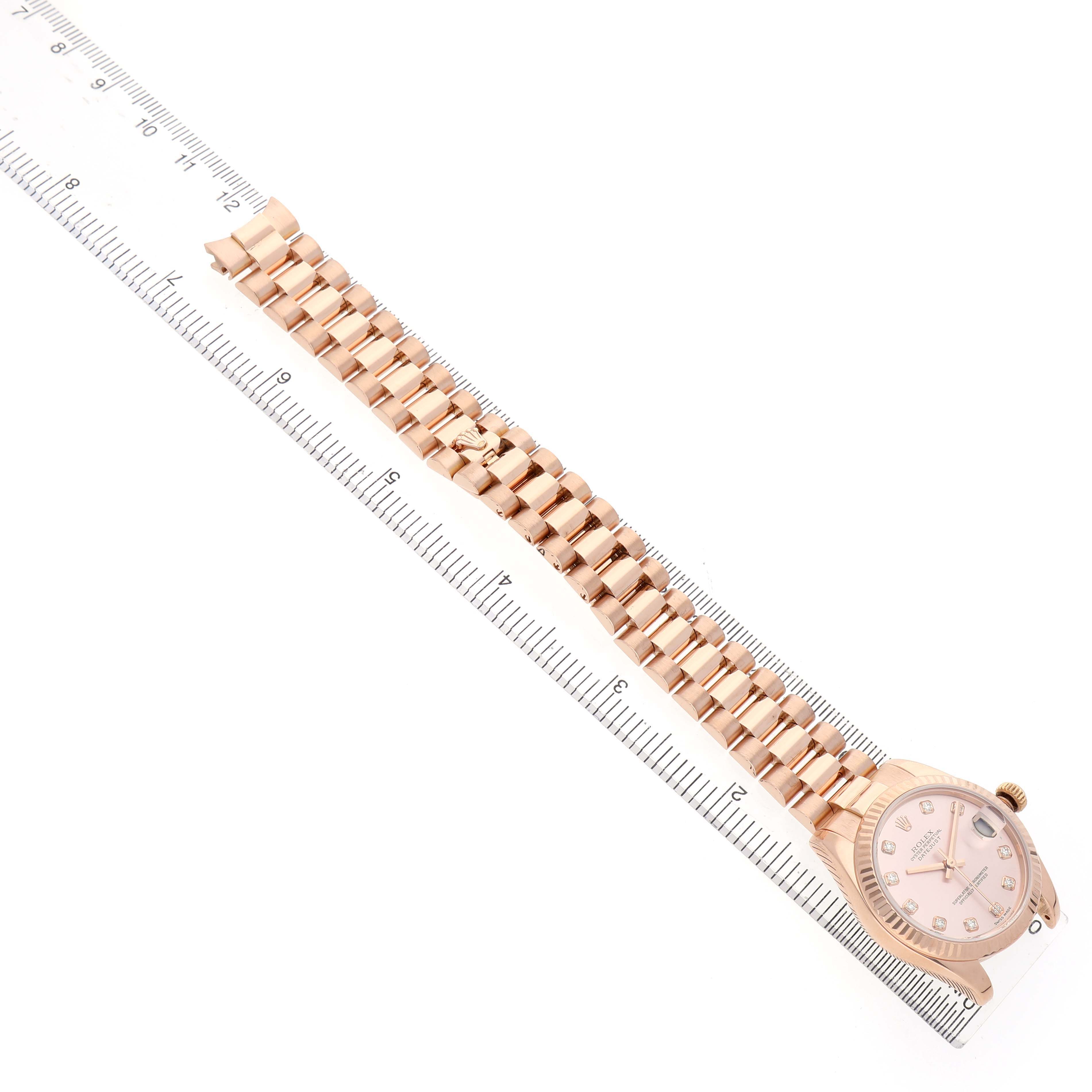 The Rolex President 178275 Women's Rose Gold Pink Dial model watch is shown from a top-down angle, highlighting the bracelet and face alongside a ruler for scale.