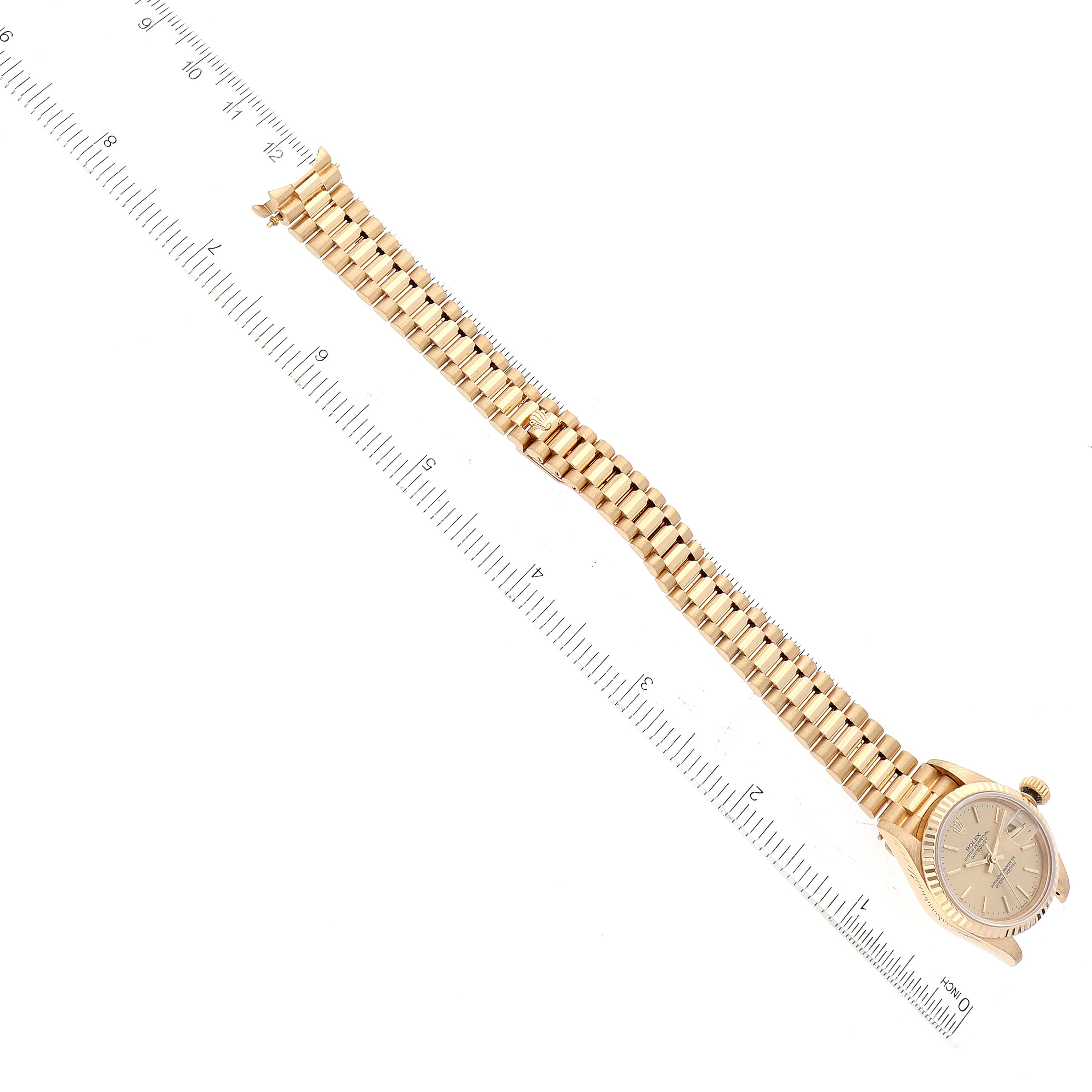 The image shows the Rolex President 69178 Women
s Yellow Gold Champagne Dial 69178 Women
s Yellow Gold Champagne Dial model watch laid flat from an overhead angle, including the face and gold bracelet next to a ruler.