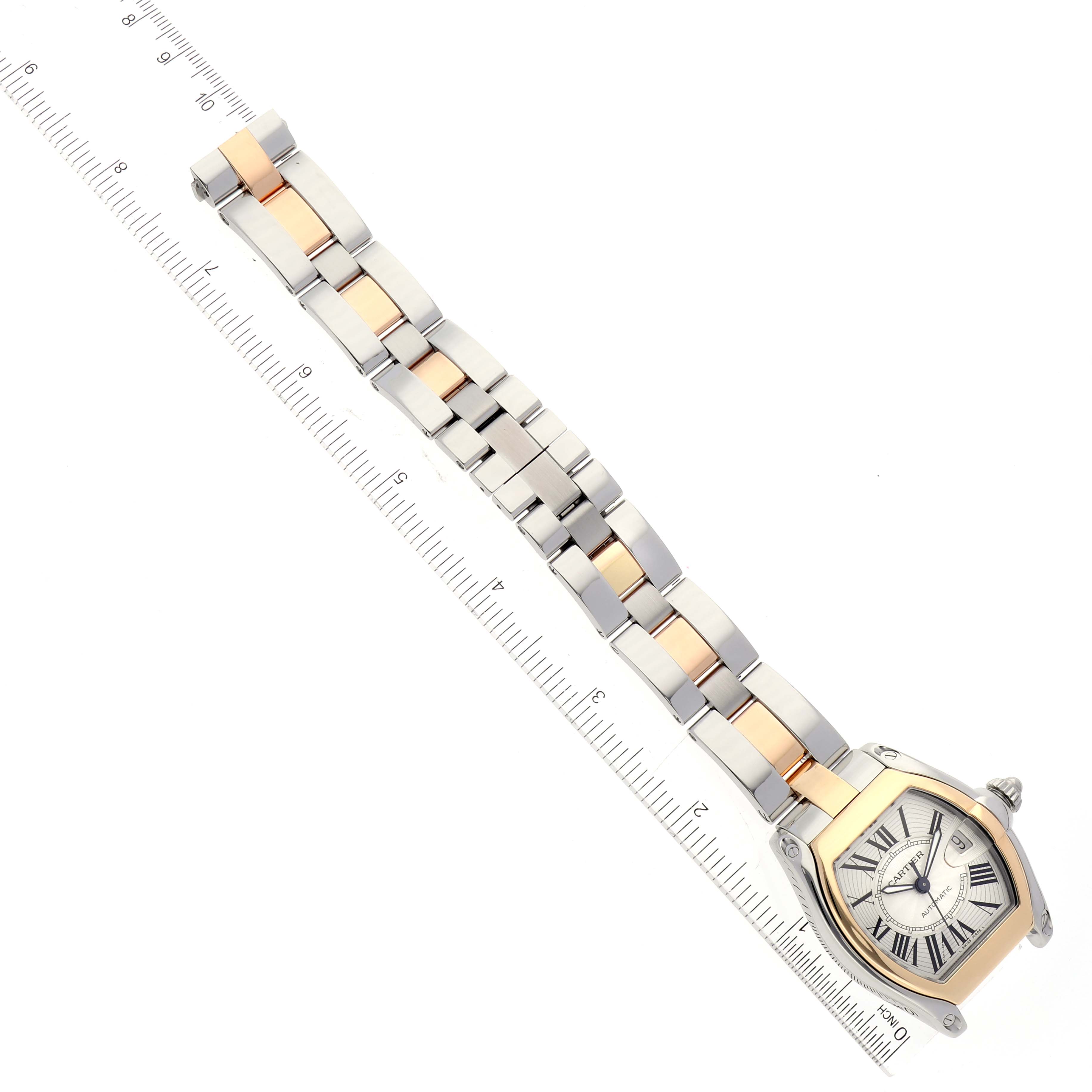 The image shows a top-down view of a Cartier Roadster W62031Y4 Men
s Steel and Gold (two tone) Silver Dial W62031Y4 Men
s Steel and Gold (two tone) Silver Dial watch, highlighting its face and two-tone metal bracelet, next to a ruler.