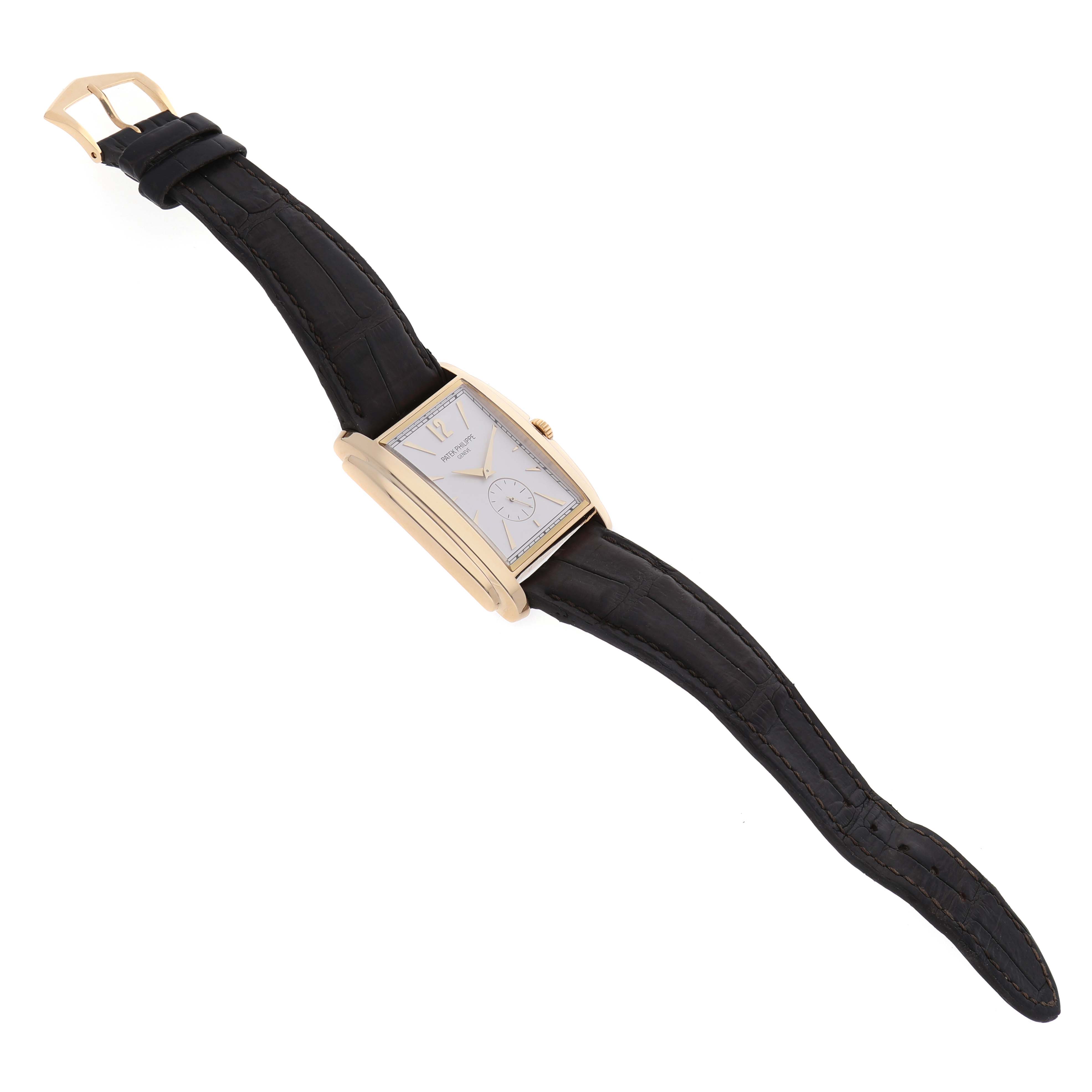 The Patek Philippe Gondolo 5124J-001 Men's Yellow Gold Silver Dial watch is shown at an oblique angle, highlighting the rectangular case, black strap, and gold buckle.