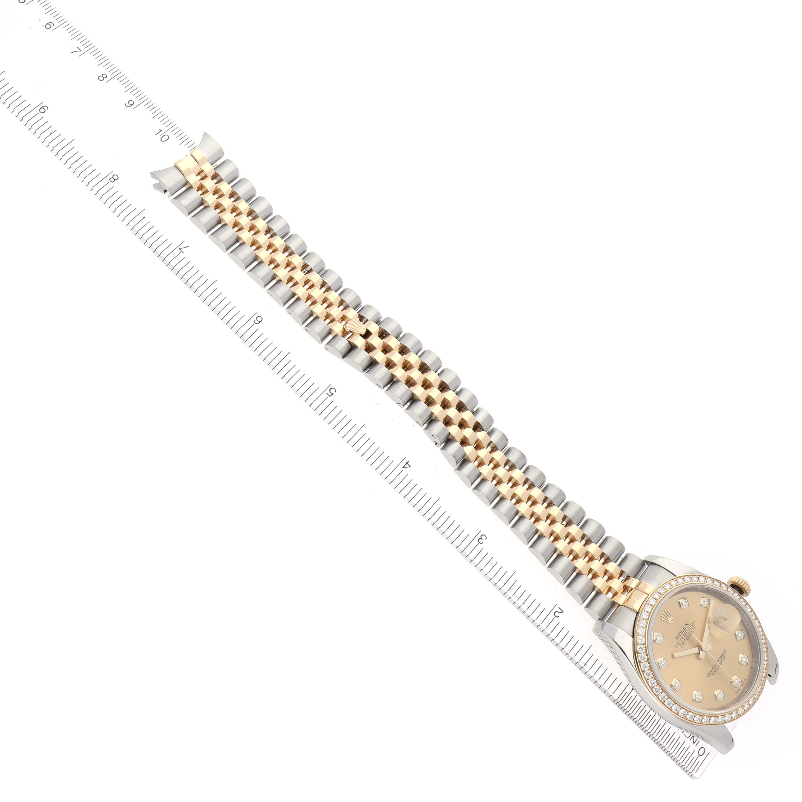 The Rolex Datejust 116243 Men
s Steel and Gold (two tone) Champagne Dial watch is shown from an overhead angle, featuring its bezel, dial, and jubilee bracelet alongside a ruler.