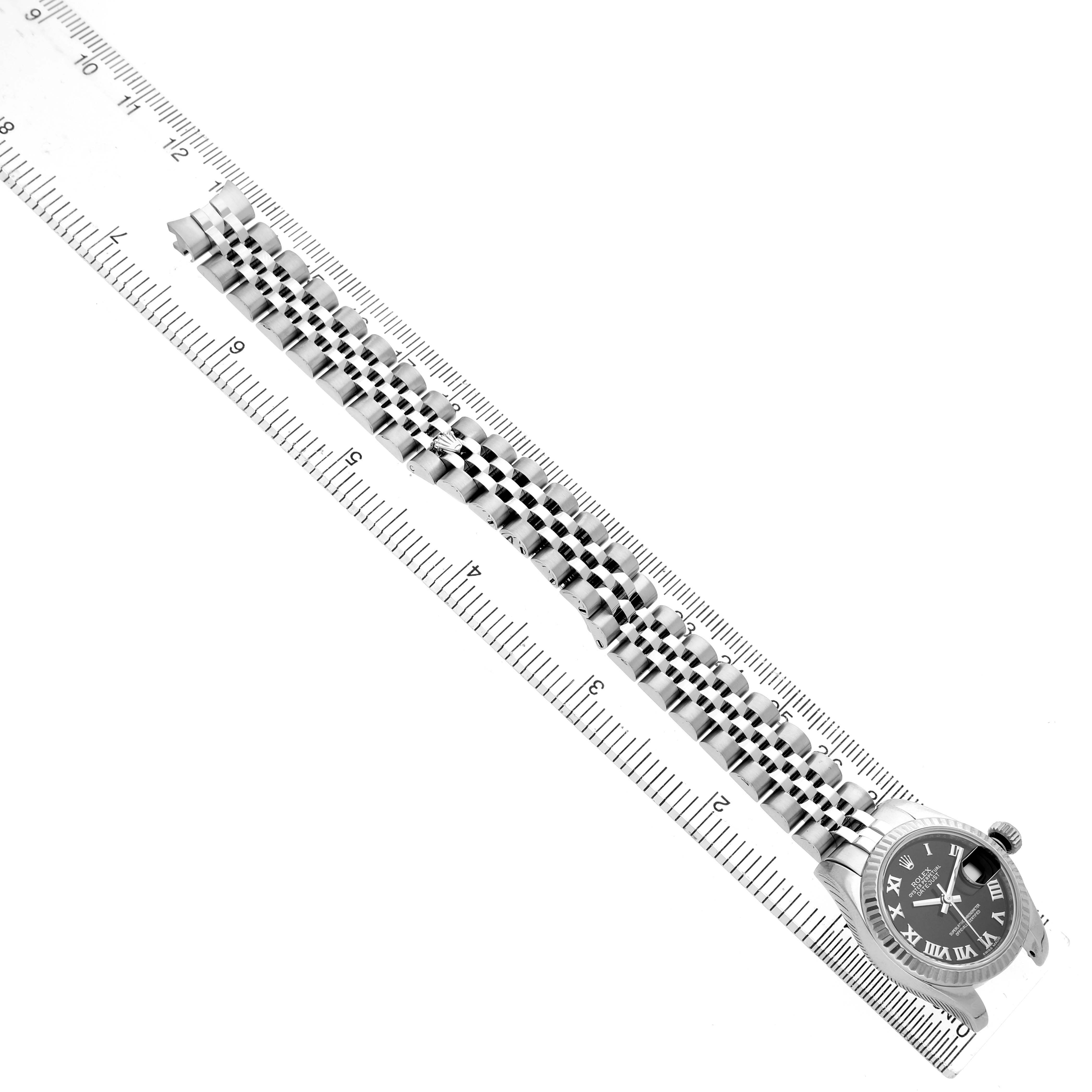 The image shows a Rolex Datejust 179174 Women's Stainless Steel Black Dial watch from an overhead angle, displaying the face and entire bracelet aligned next to a ruler.