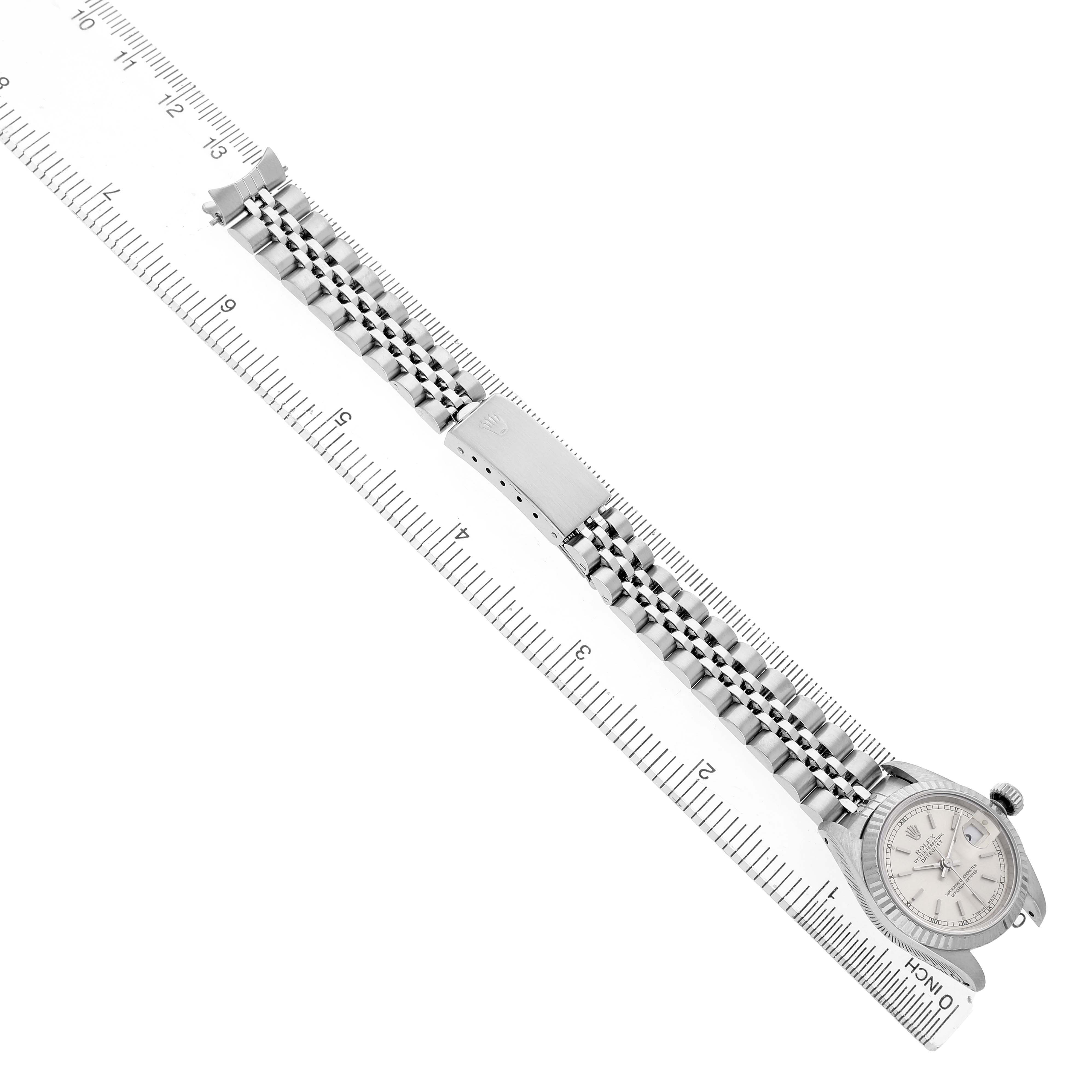 The Rolex Datejust 69174 Women's Stainless Steel Silver Dial watch is shown from an angled top view, highlighting the face, bracelet, and clasp beside a ruler.