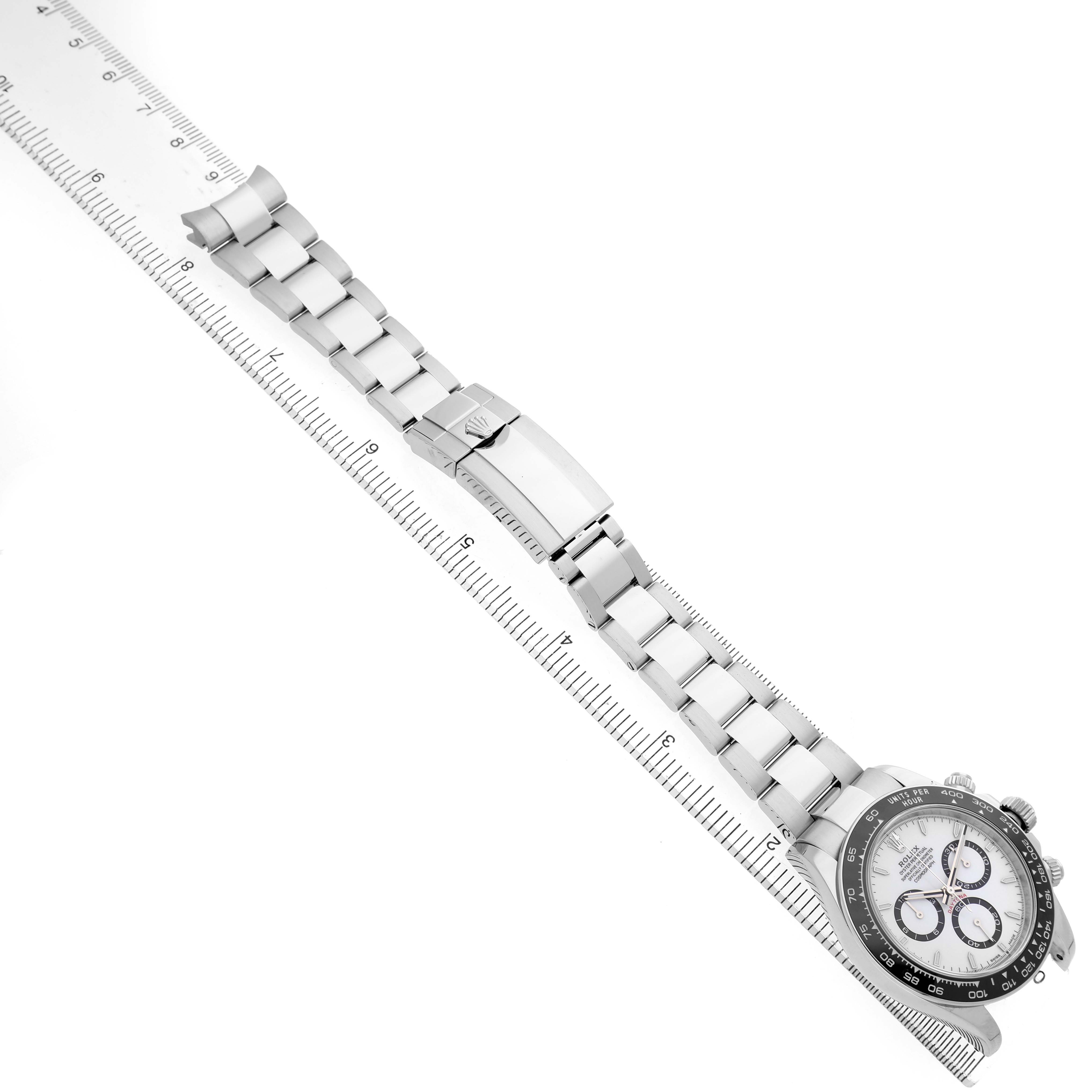 The Rolex Daytona 126500 Men's Stainless Steel White Dial watch is shown from an overhead view, displaying the face, bezel, bracelet, and clasp along with a ruler for scale.