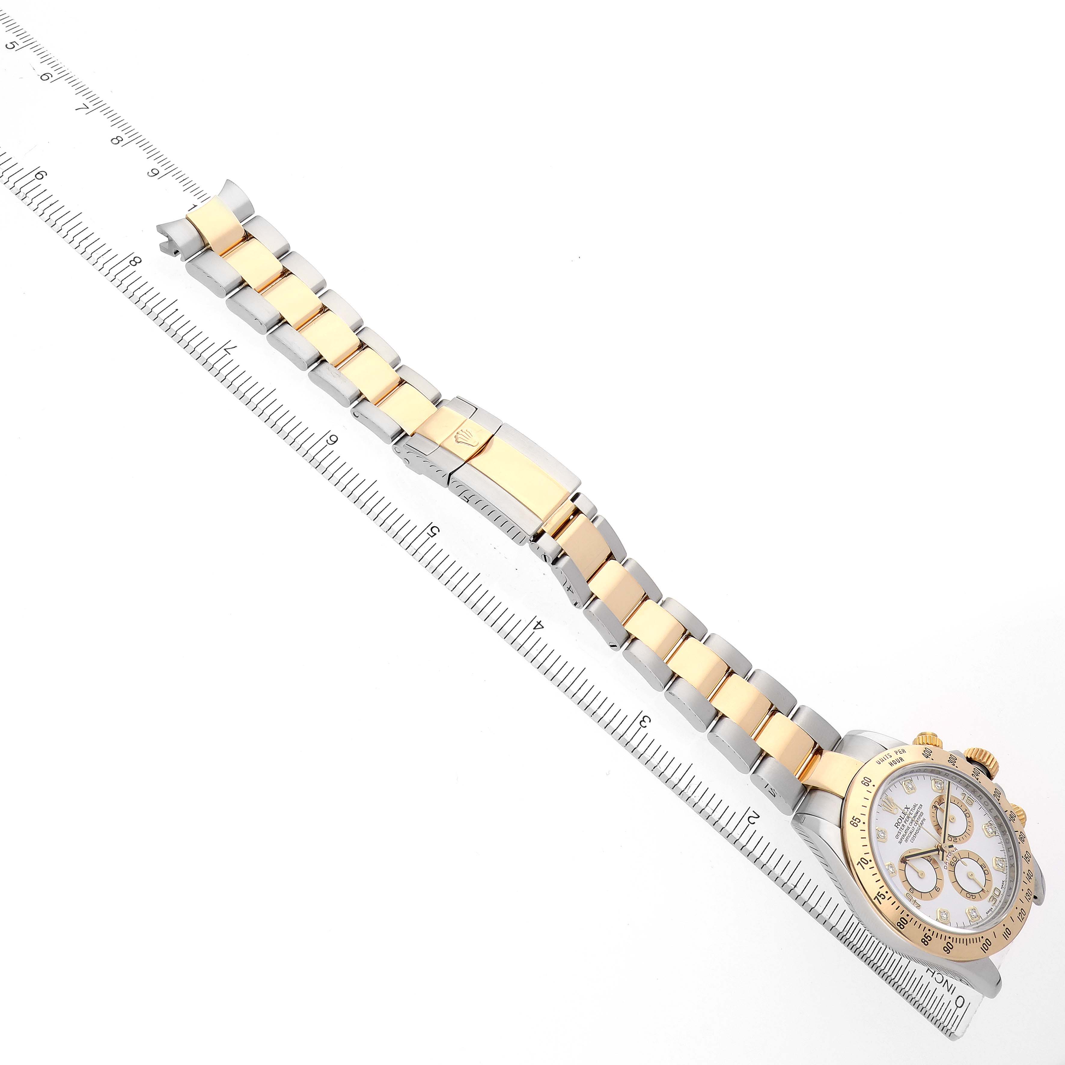 The Rolex Daytona 116523 Men's Steel and Gold (two tone) White Dial watch is shown from an angle displaying its full bracelet and face, placed next to a ruler for scale.