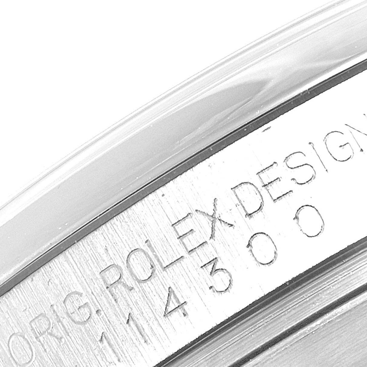 This image shows a close-up of the engraved serial number and "ROLEX DESIGN" text on the case of a Rolex Oyster Perpetual 114300 Men's Stainless Steel Blue Dial 114300 Men's Stainless Steel Blue Dial watch.