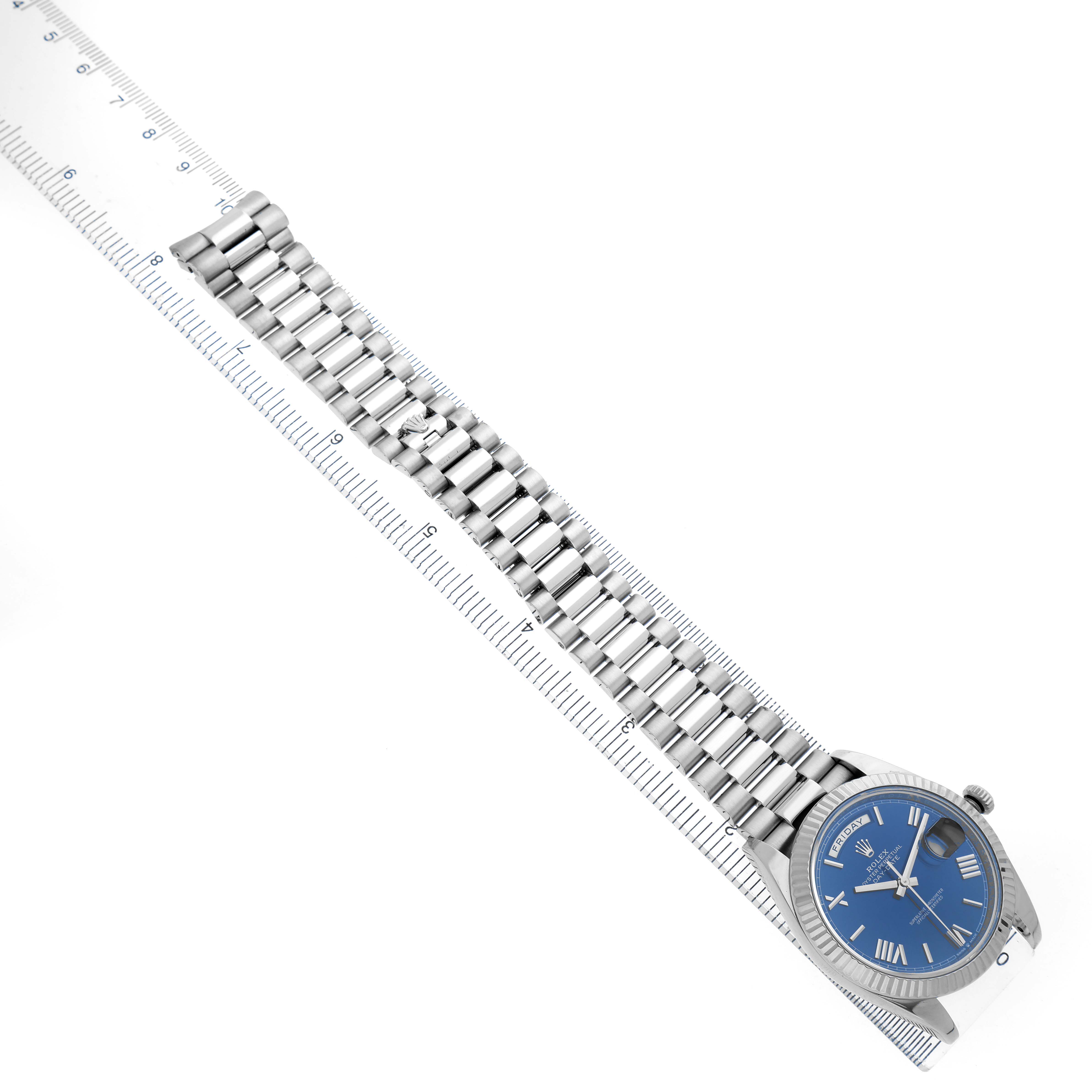 The Rolex President 228239 Men's White Gold Blue Dial watch is viewed from above, showing its blue dial and full bracelet alongside a ruler.