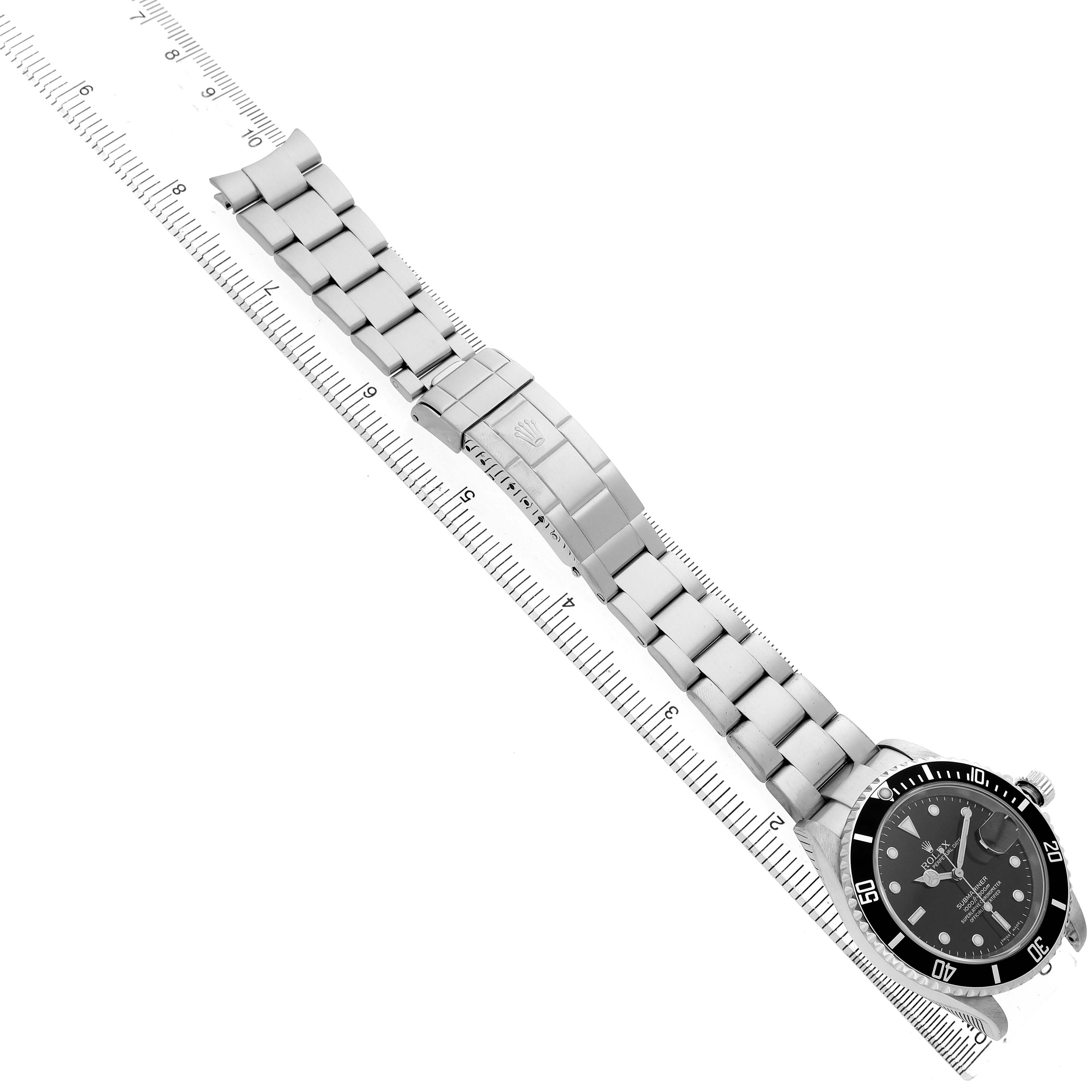 The Rolex Submariner 16610 Men's Stainless Steel Black Dial watch is shown from a top-down angle, displaying the full bracelet and face alongside a ruler for scale.