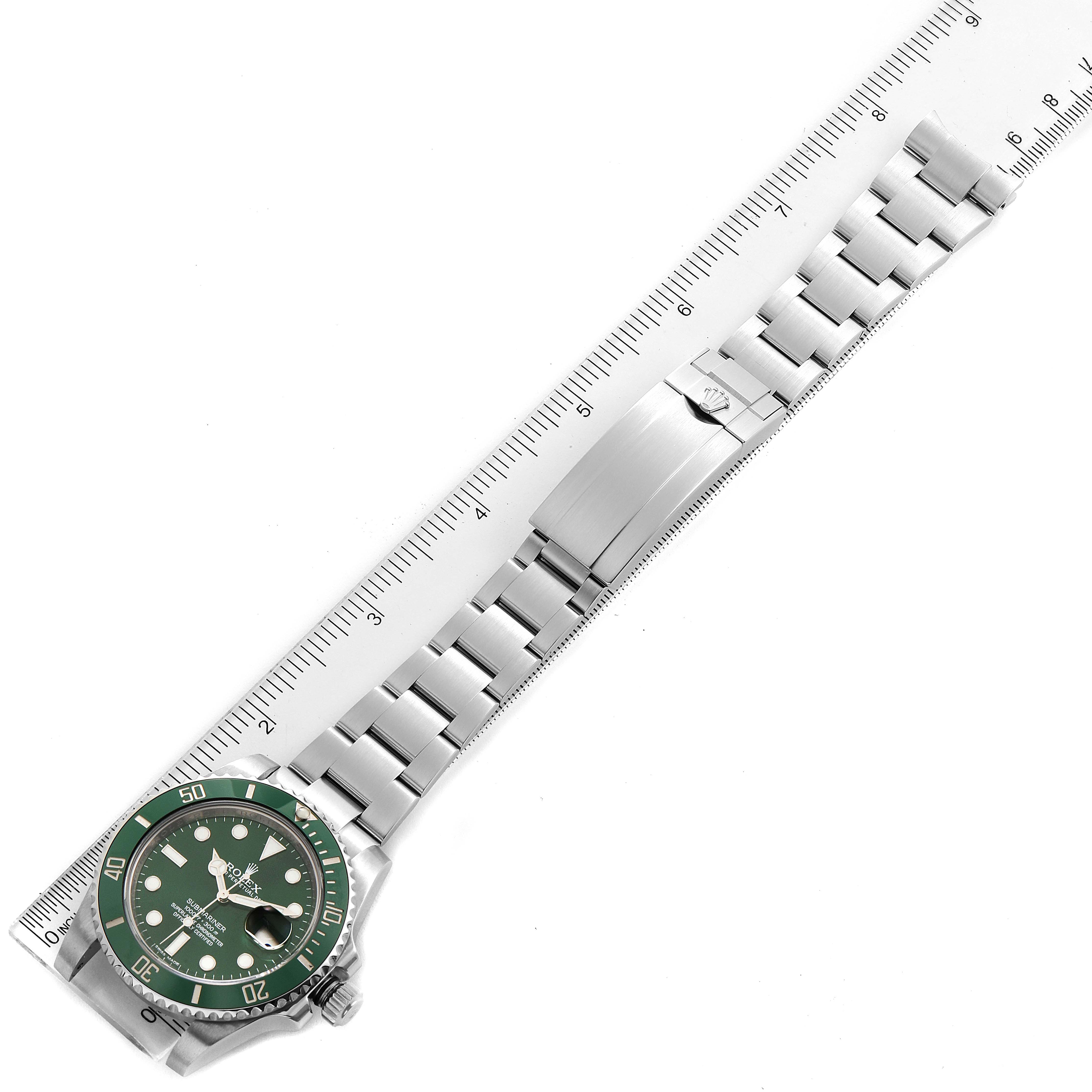 This image features a top-down view of a Rolex Submariner 116610LV Men's Stainless Steel Green Dial 116610LV Men's Stainless Steel Green Dial watch with a green bezel and silver bracelet set against a ruler for measurement.