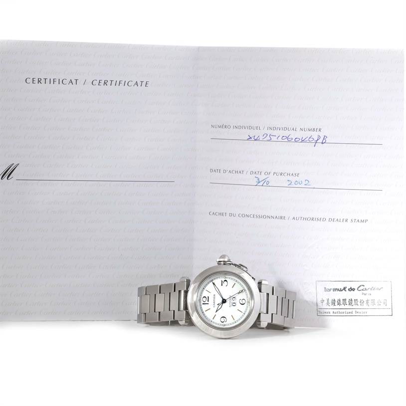 This image shows the Cartier Pasha W31044M7 Men
s Stainless Steel Silver Dial W31044M7 Men
s Stainless Steel Silver Dial watch laid flat with its certificate displayed behind it.