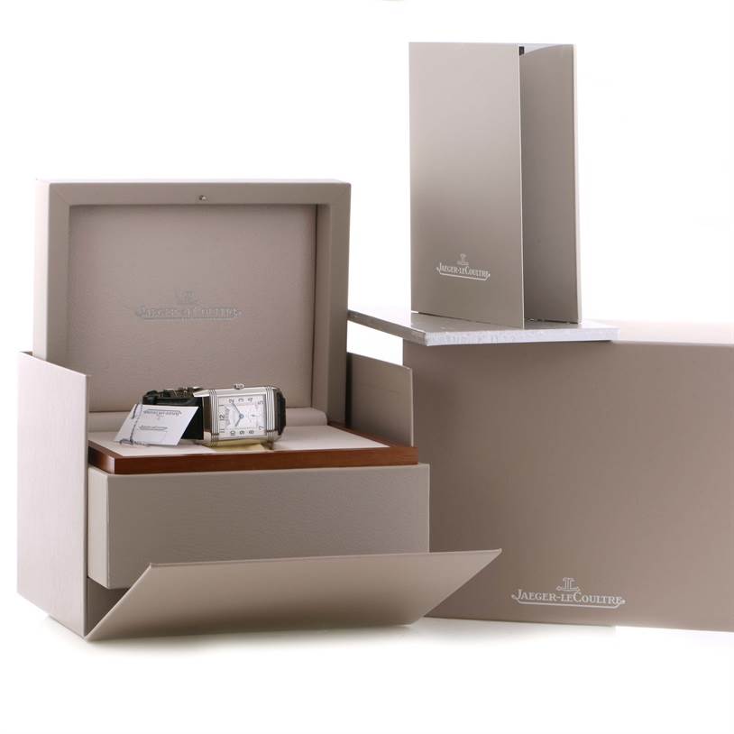 The image shows a Jaeger-LeCoultre Reverso watch in its open box from a front angle, with accompanying packaging and manuals.
