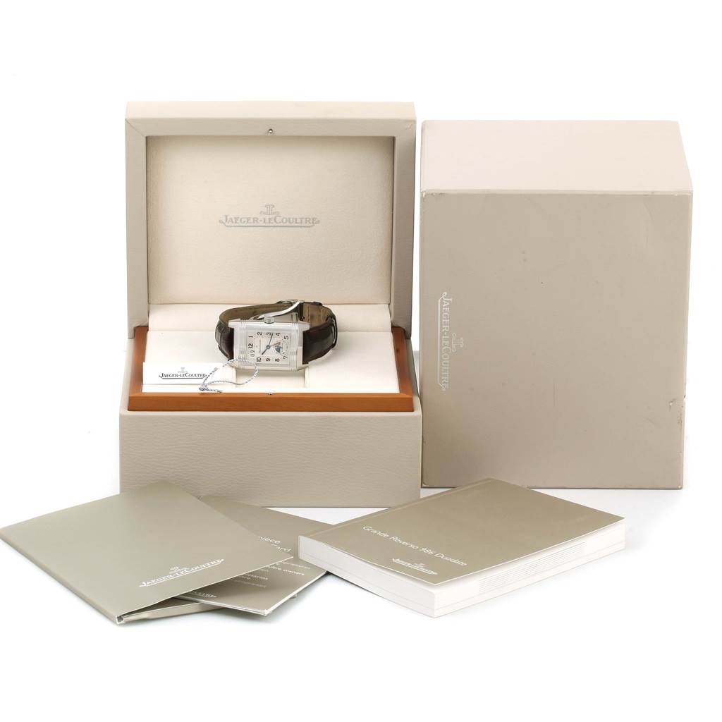 The image shows a Jaeger-LeCoultre Reverso watch in an open box with manuals and additional packaging.