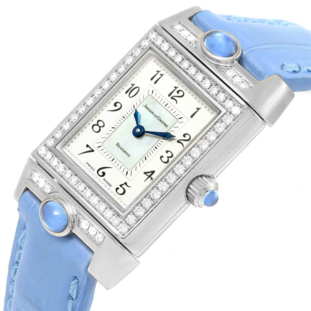 The Jaeger-LeCoultre Reverso watch is shown at a slight angle, highlighting its face, diamond bezel, and light blue strap.