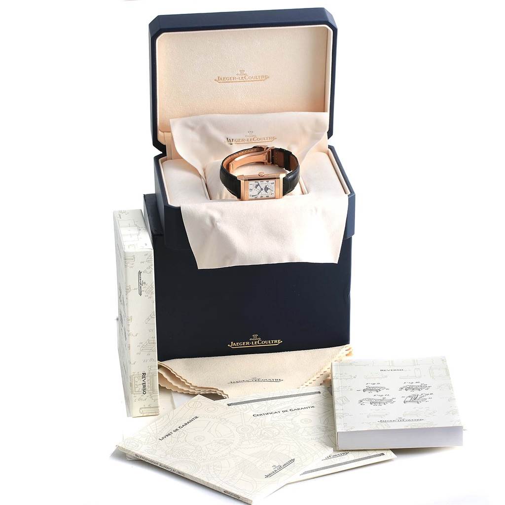 This image shows a Jaeger LeCoultre Reverso Q3042420 Men's Rose Gold Silver Dial Q3042420 Men's Rose Gold Silver Dial watch in its box with accompanying booklets and cleaning cloth.