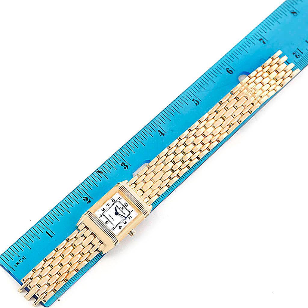 The image shows a Jaeger LeCoultre Reverso Q2611110 Women's Yellow Gold Silver Dial Q2611110 Women's Yellow Gold Silver Dial watch laid flat against a ruler, featuring the watch face and metal bracelet.