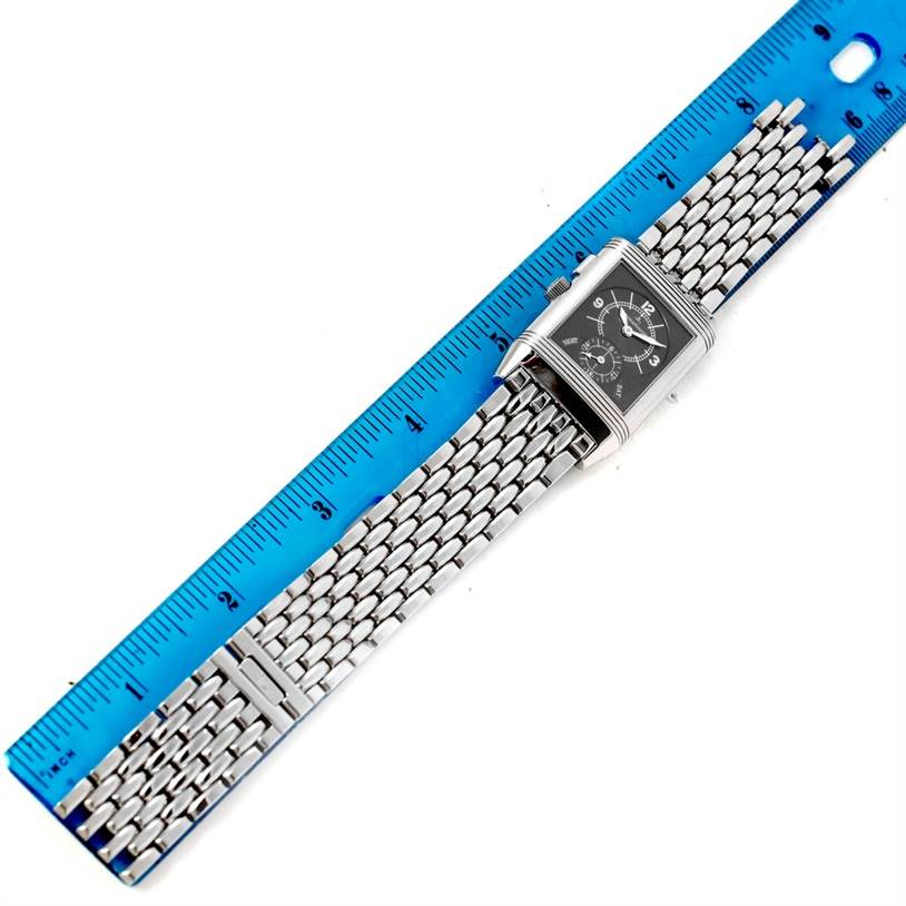 The Jaeger-LeCoultre Reverso watch is shown from a top-down angle, displaying the face and metal bracelet alongside a ruler.