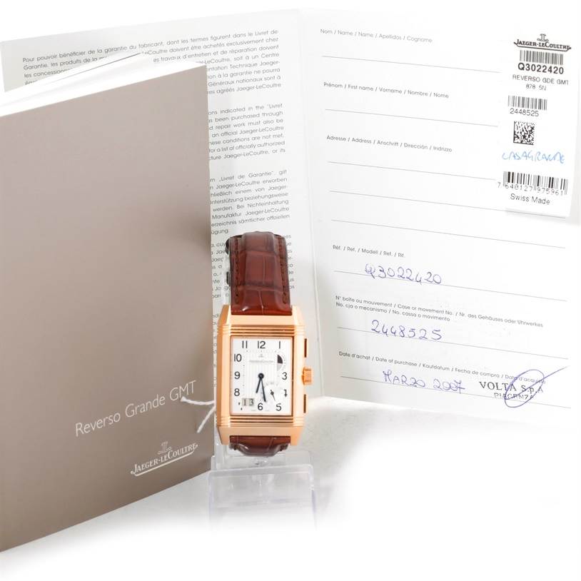 The image shows the front view of a Jaeger LeCoultre Reverso 240.2.18 Men
s Rose Gold Silver Dial 240.2.18 Men
s Rose Gold Silver Dial Grande GMT with its brown leather strap, alongside its papers and box.